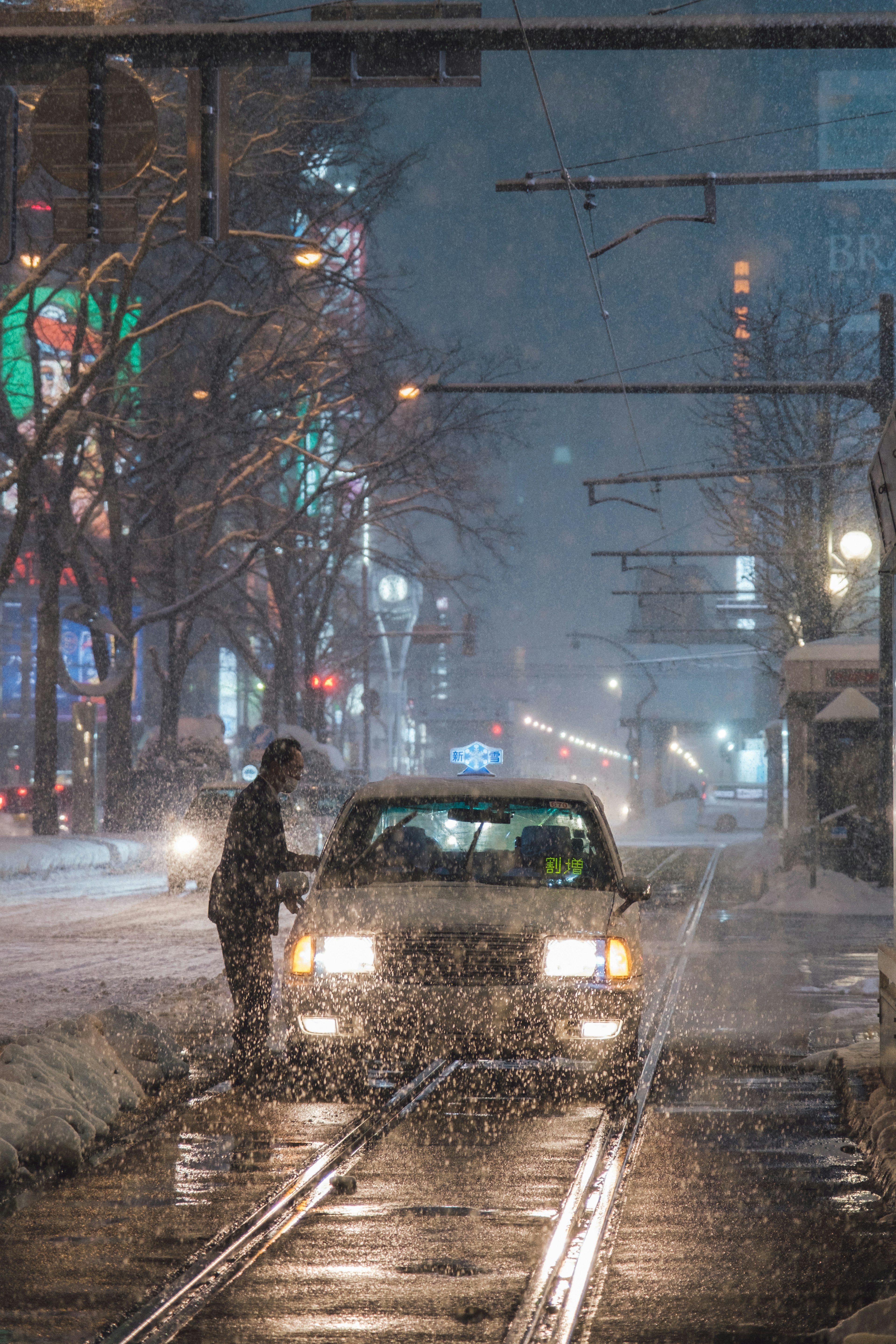 A person waiting for a taxi amidst falling snow and city lights