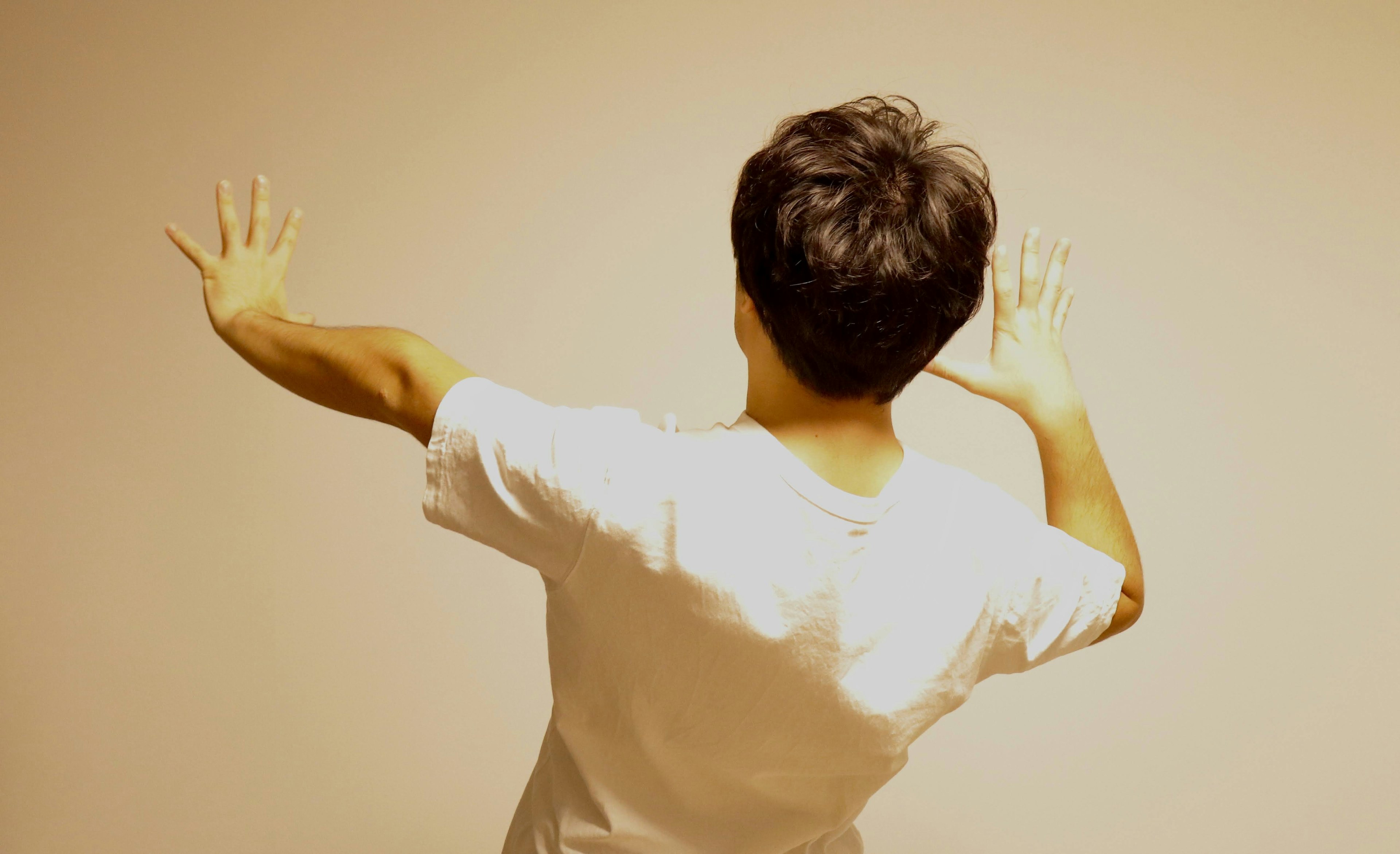 A boy in a white t-shirt facing away with hands raised