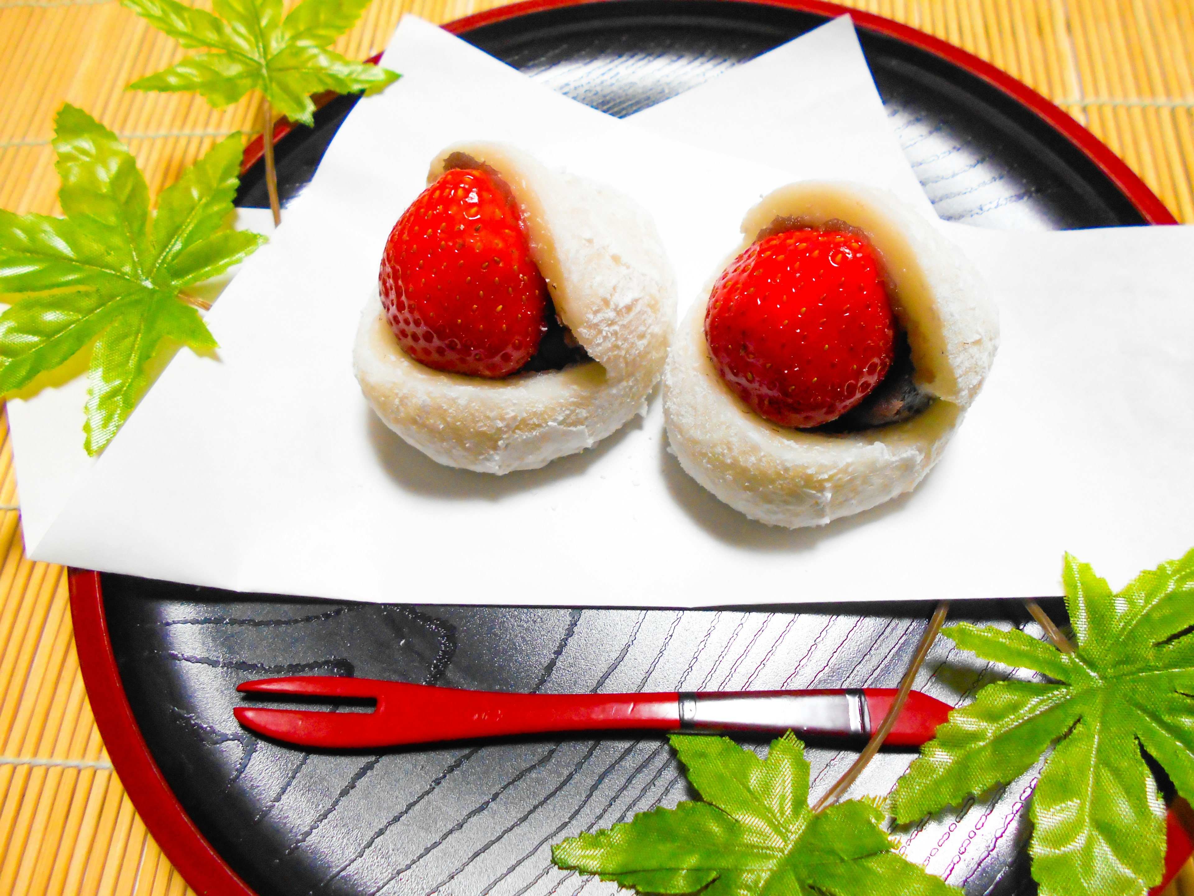 Two strawberry daifuku arranged on a traditional plate with green leaves