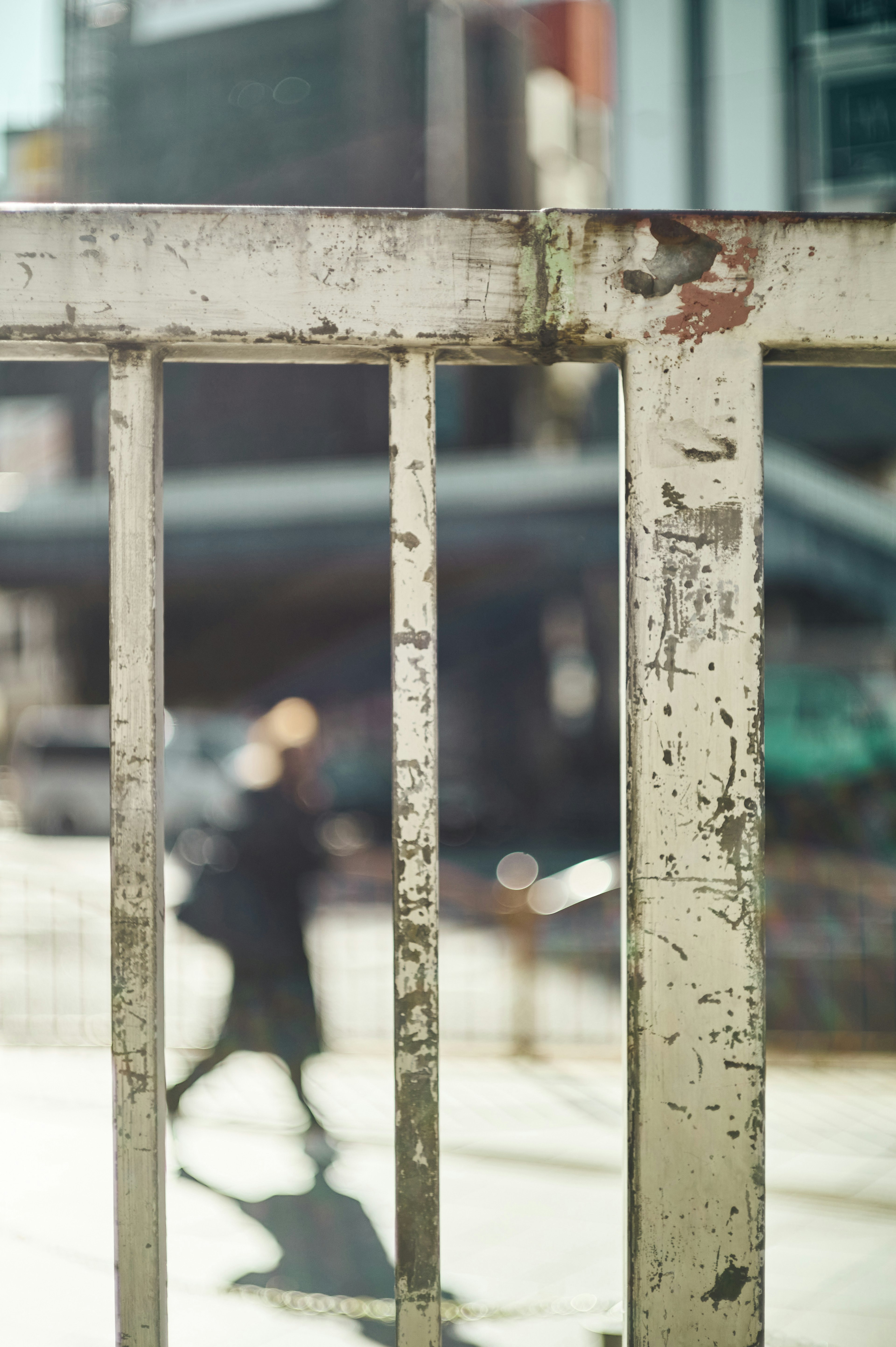 A blurred silhouette of a person walking behind an old metal fence