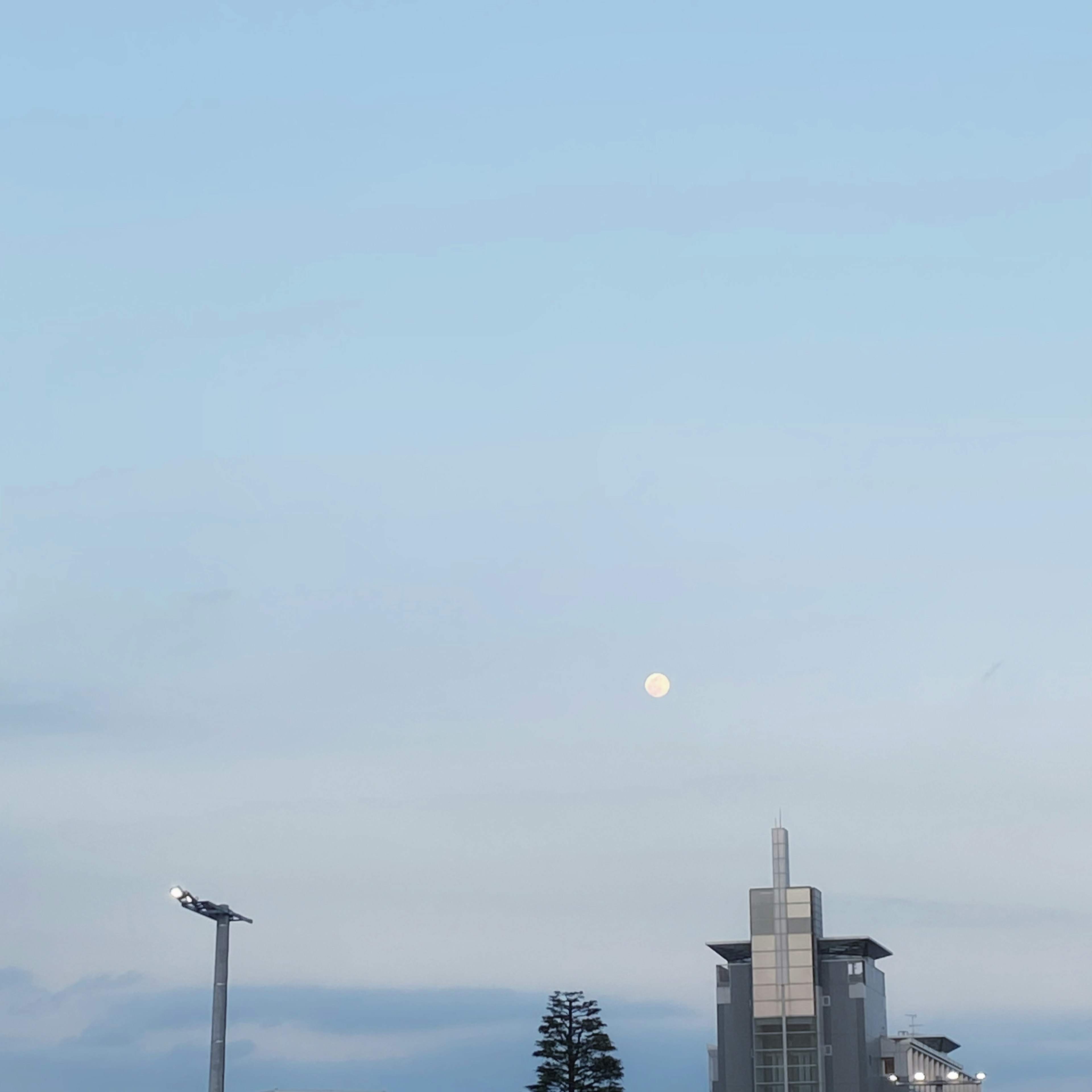 青空の下に浮かぶ月と建物のシルエット