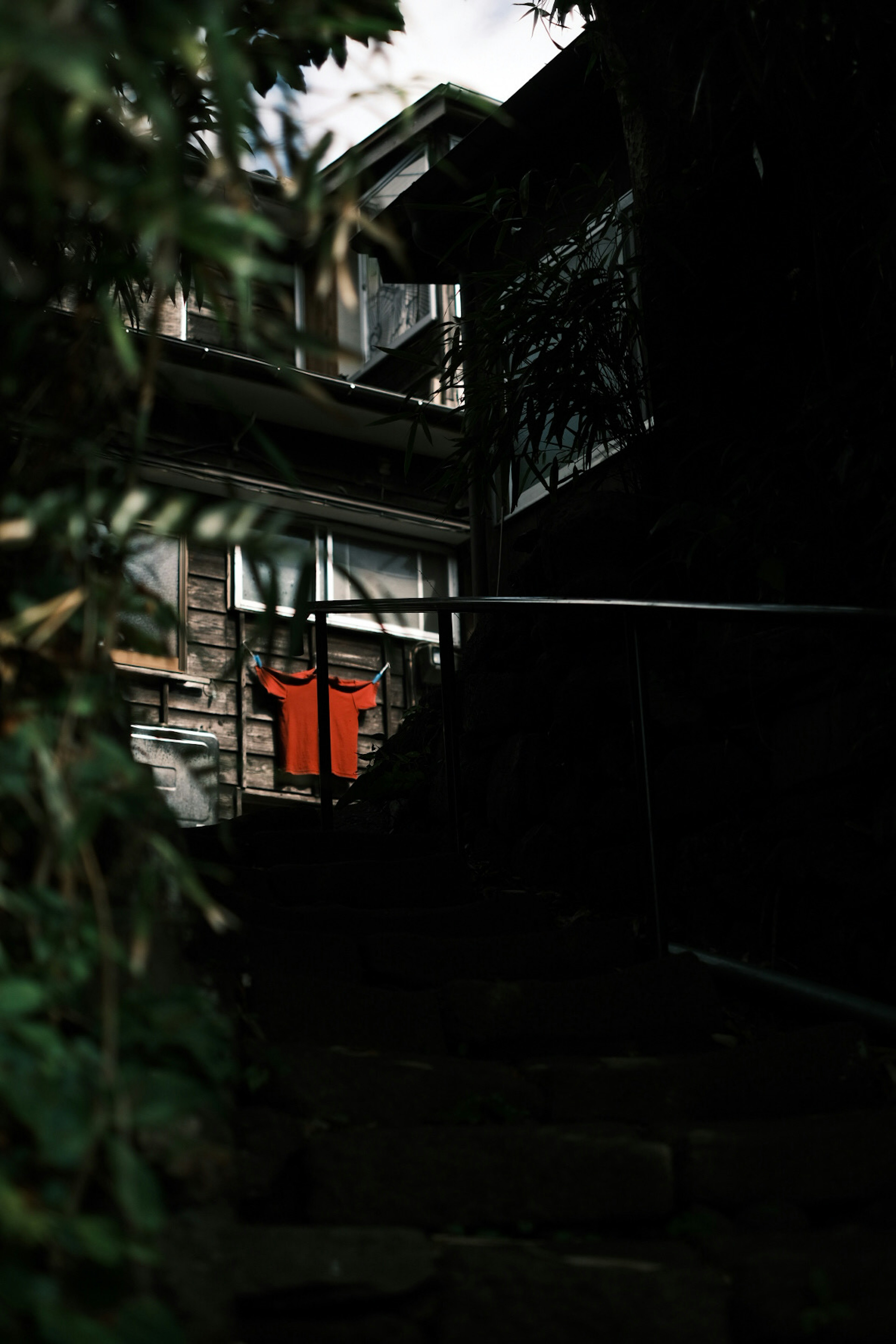 Escalier faiblement éclairé menant à une chemise orange accrochée près de vieux bâtiments