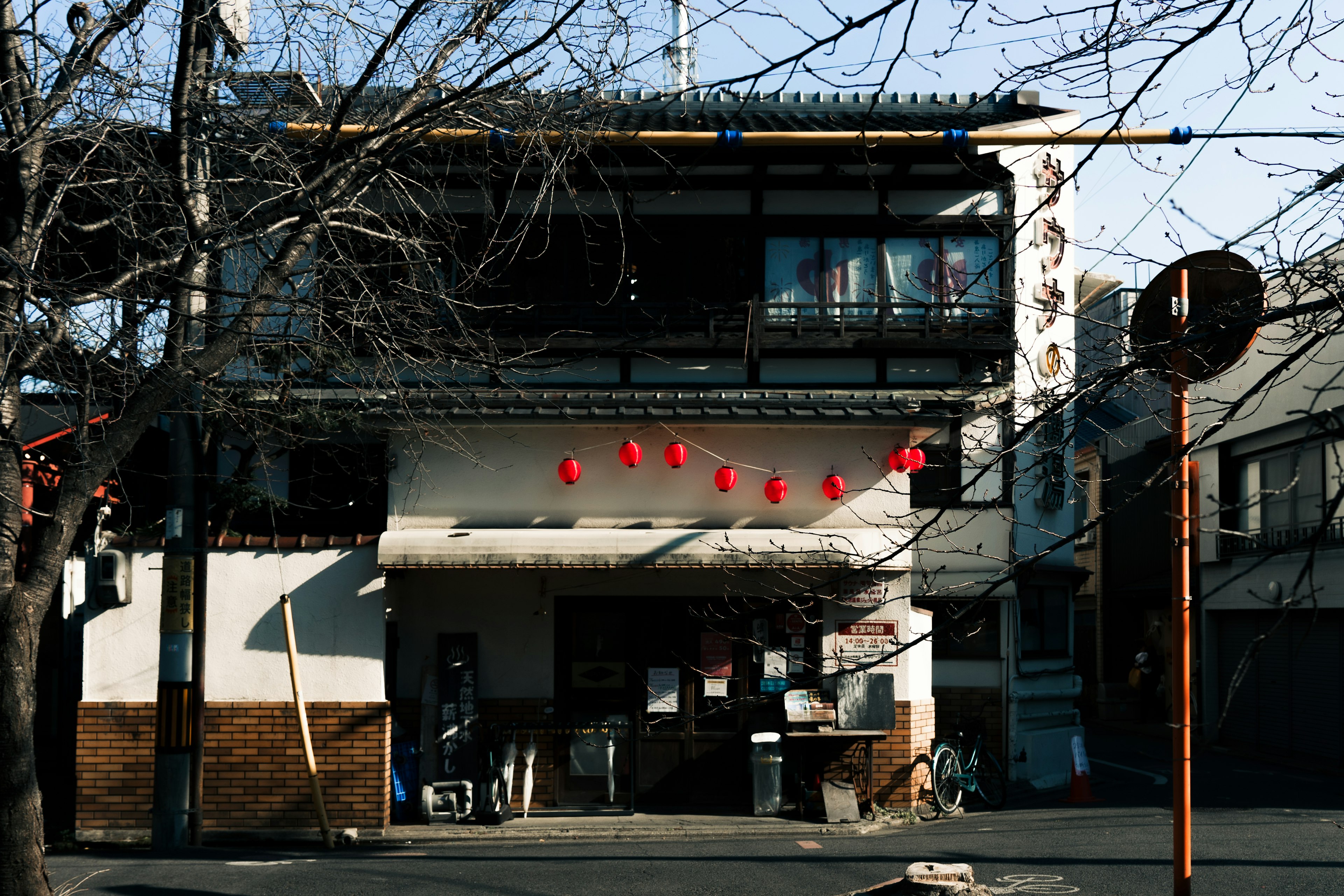 Bâtiment traditionnel japonais avec des lanternes rouges et des arbres d'hiver dénudés