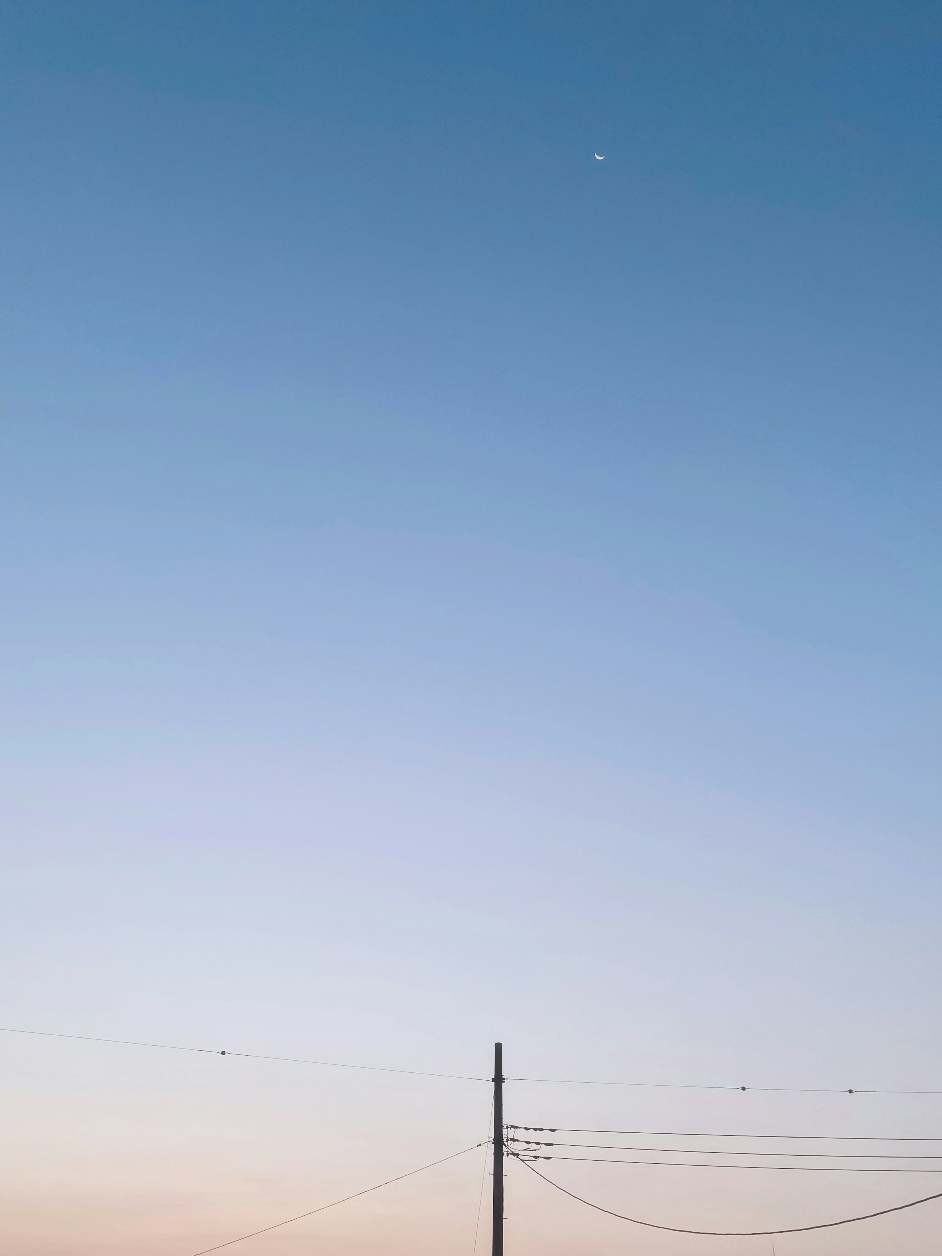 Un cielo sereno con una luna creciente y un poste de luz