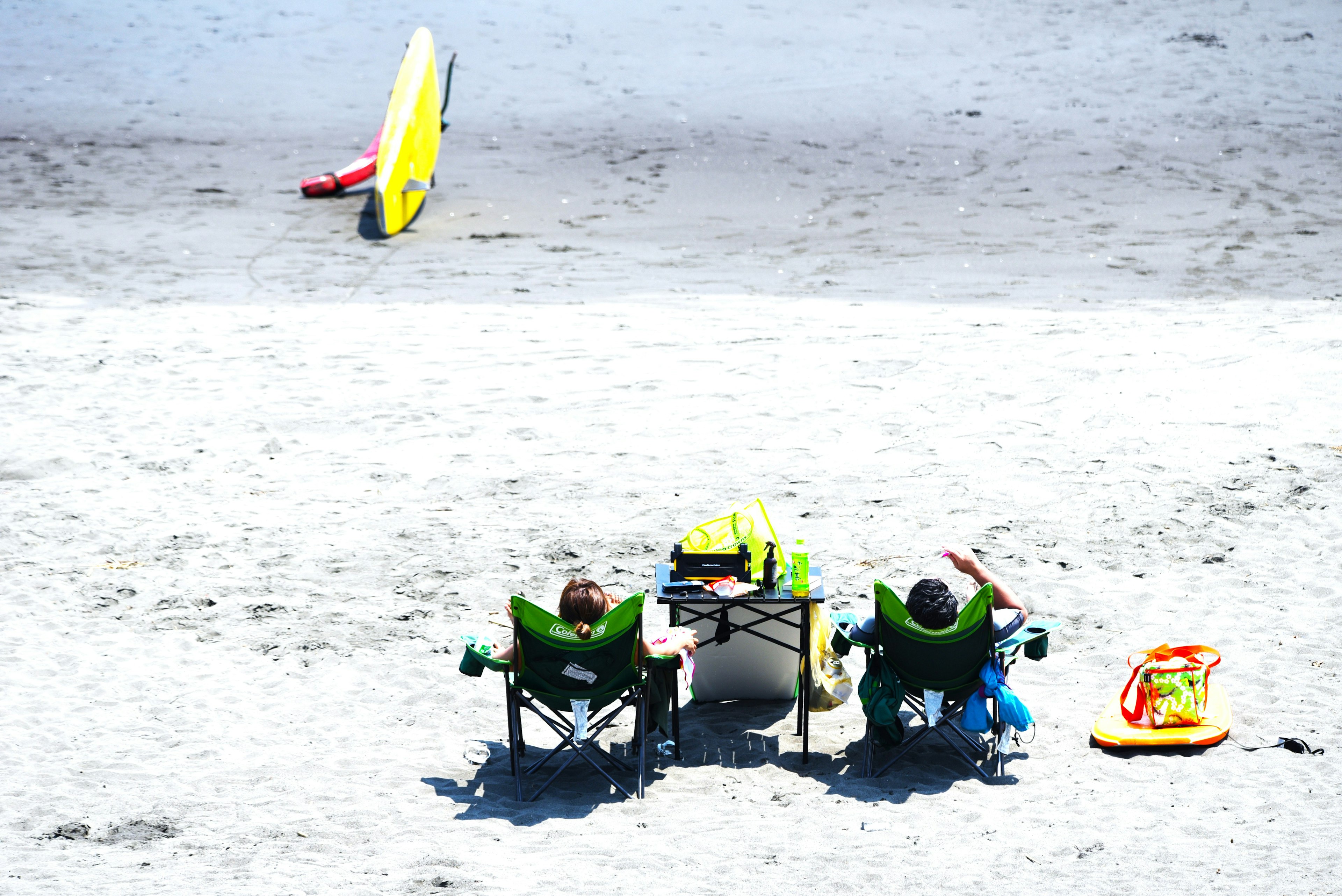 Zwei Kinder entspannen am Strand mit bunten Stühlen und einem Surfbrett