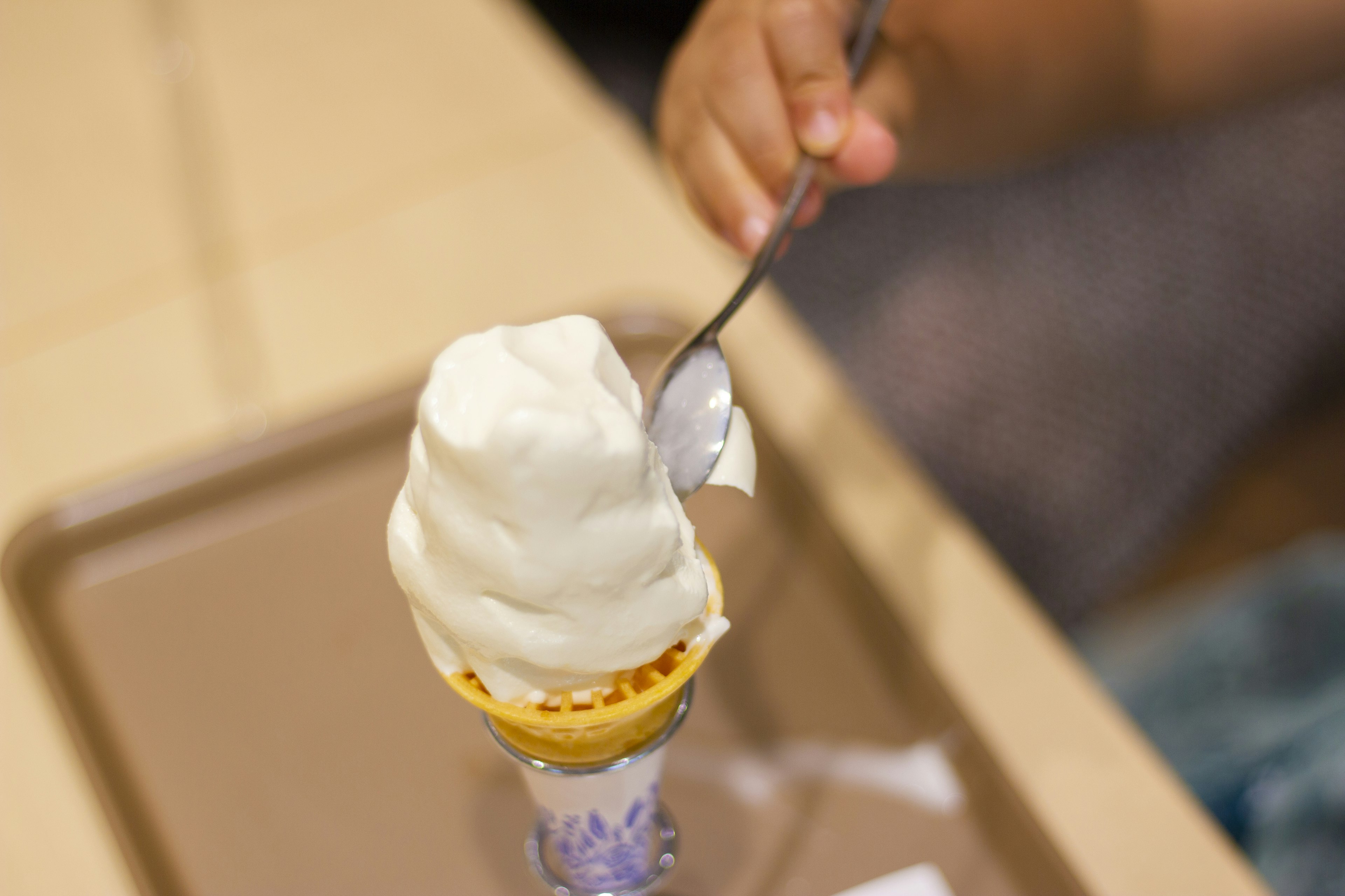 Un helado suave y cremoso encima de un cono con una mano sosteniendo una cuchara