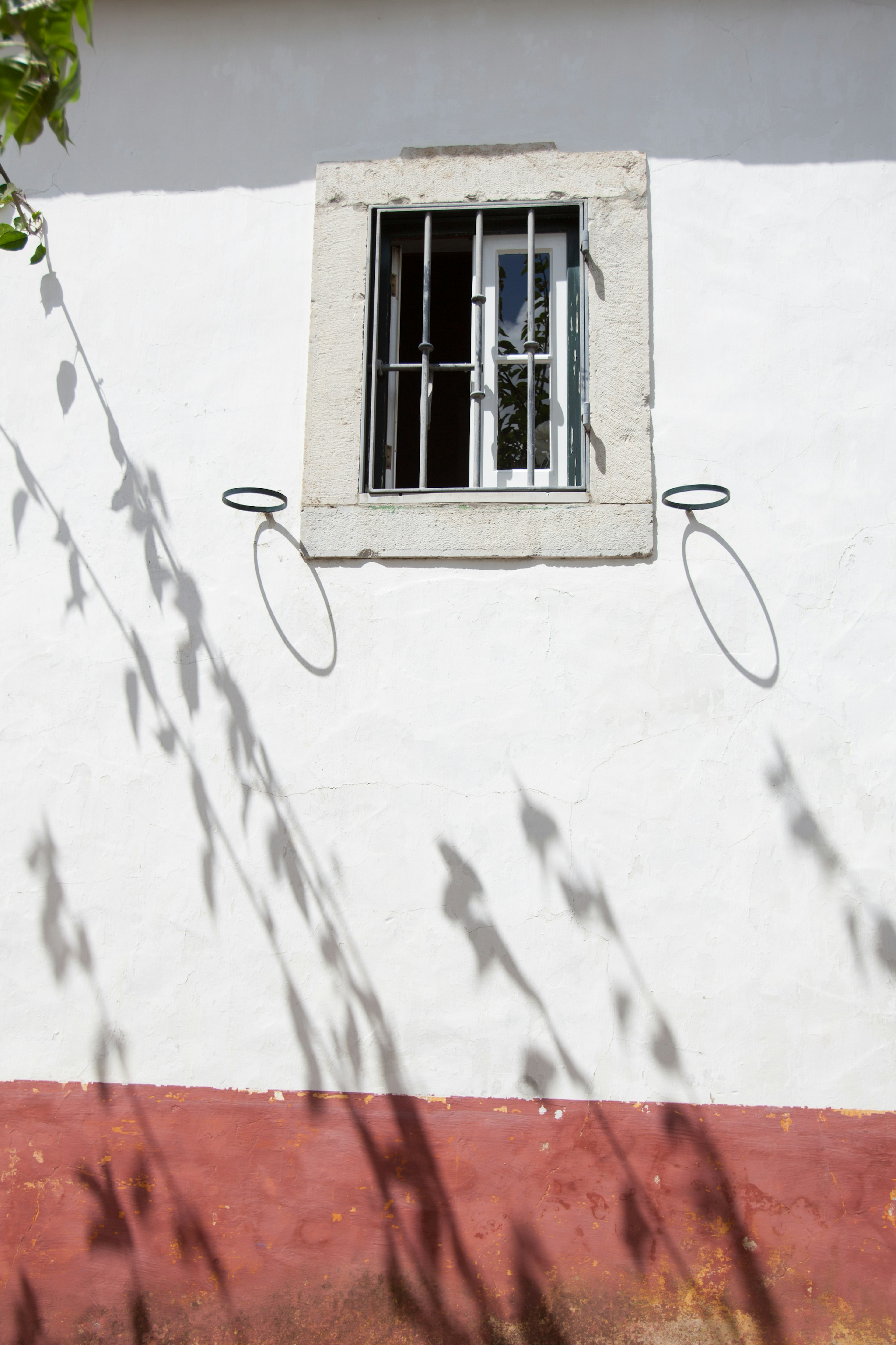 Fenster mit Gitter an einer weißen Wand, die Schatten wirft