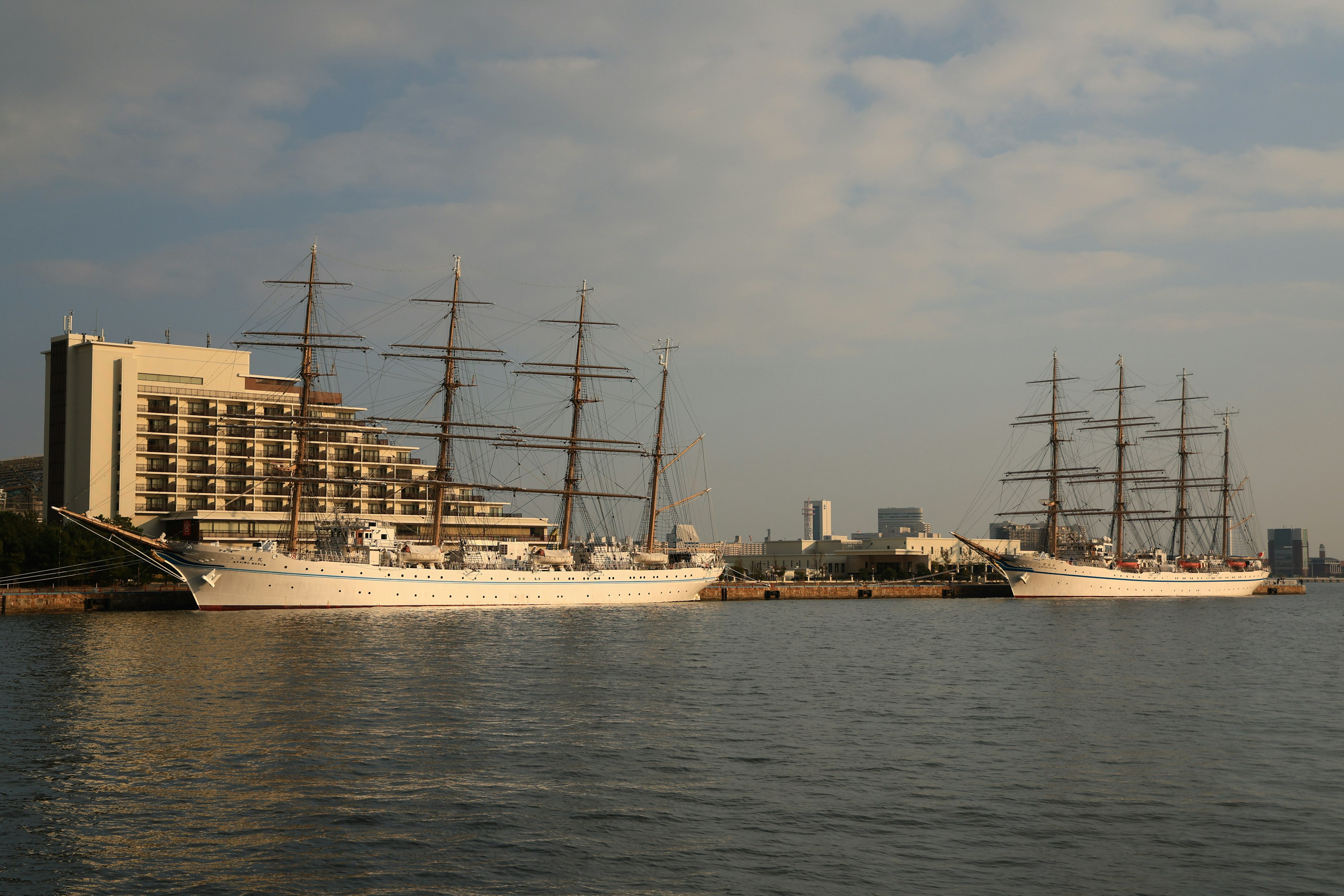 Two sailing ships on the water with a modern building in the background