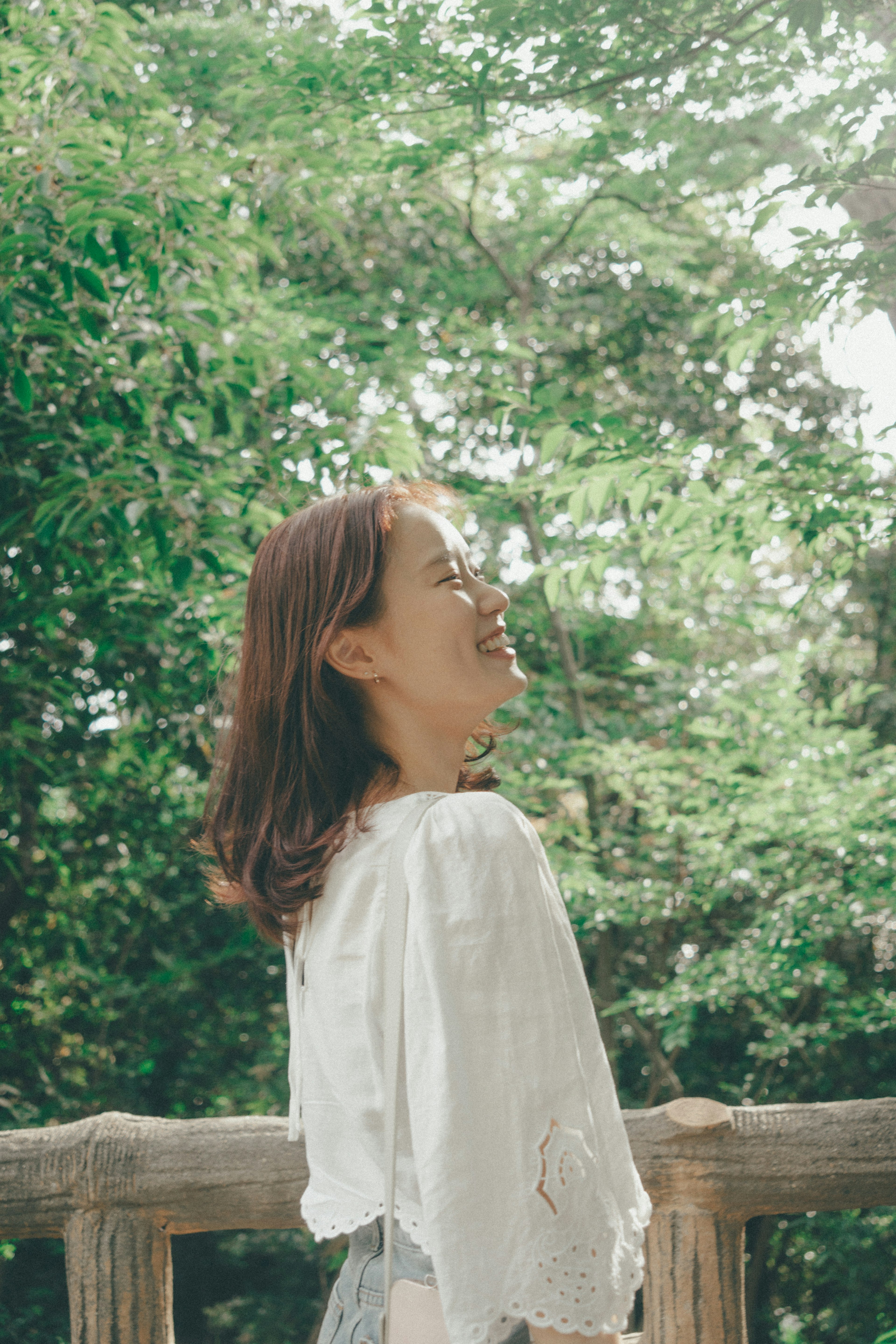 公園で微笑む女性の横顔　緑の木々と木のフェンスが背景