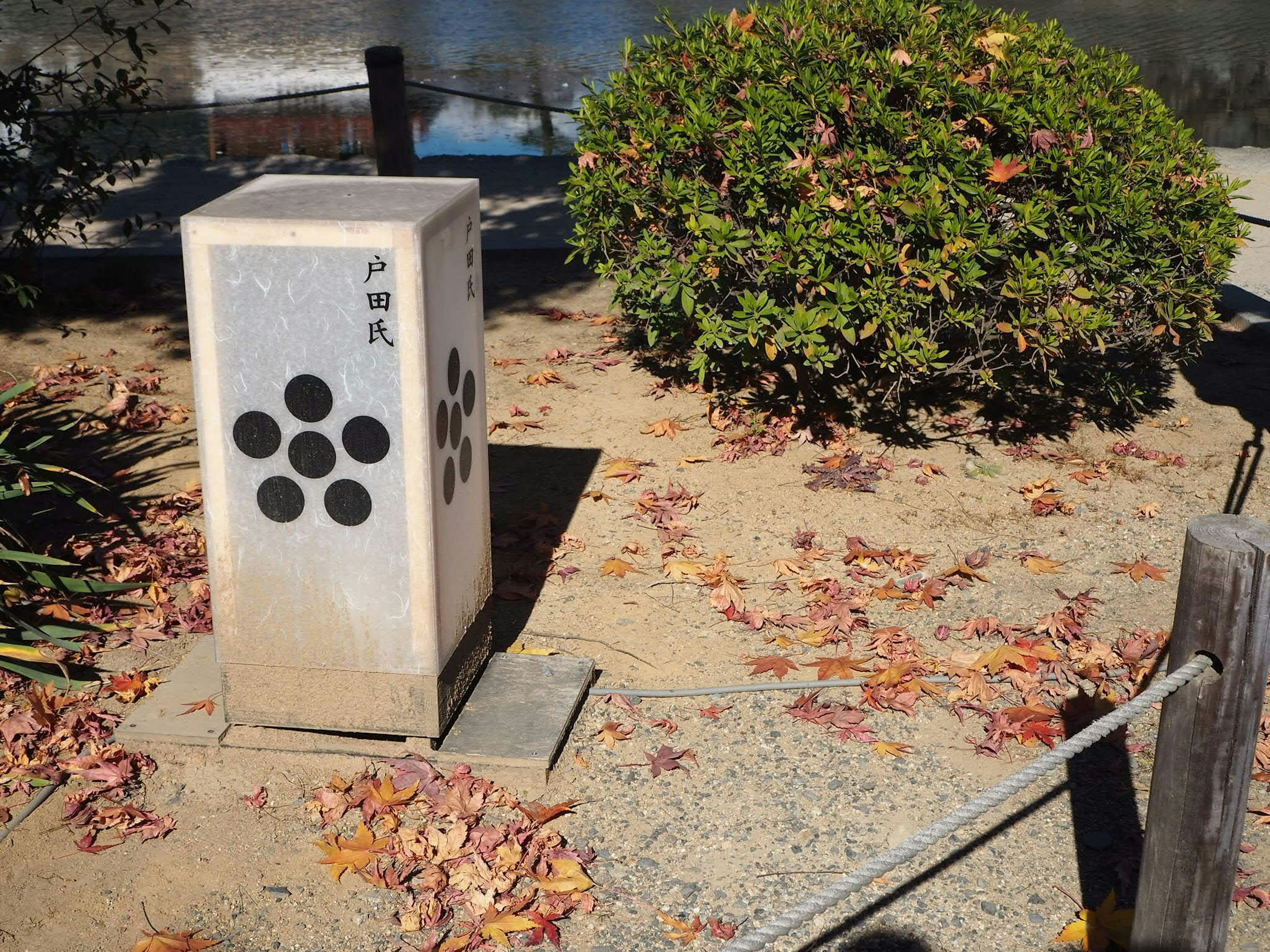 Monument en pierre dans un parc avec des plantes environnantes et des feuilles tombées