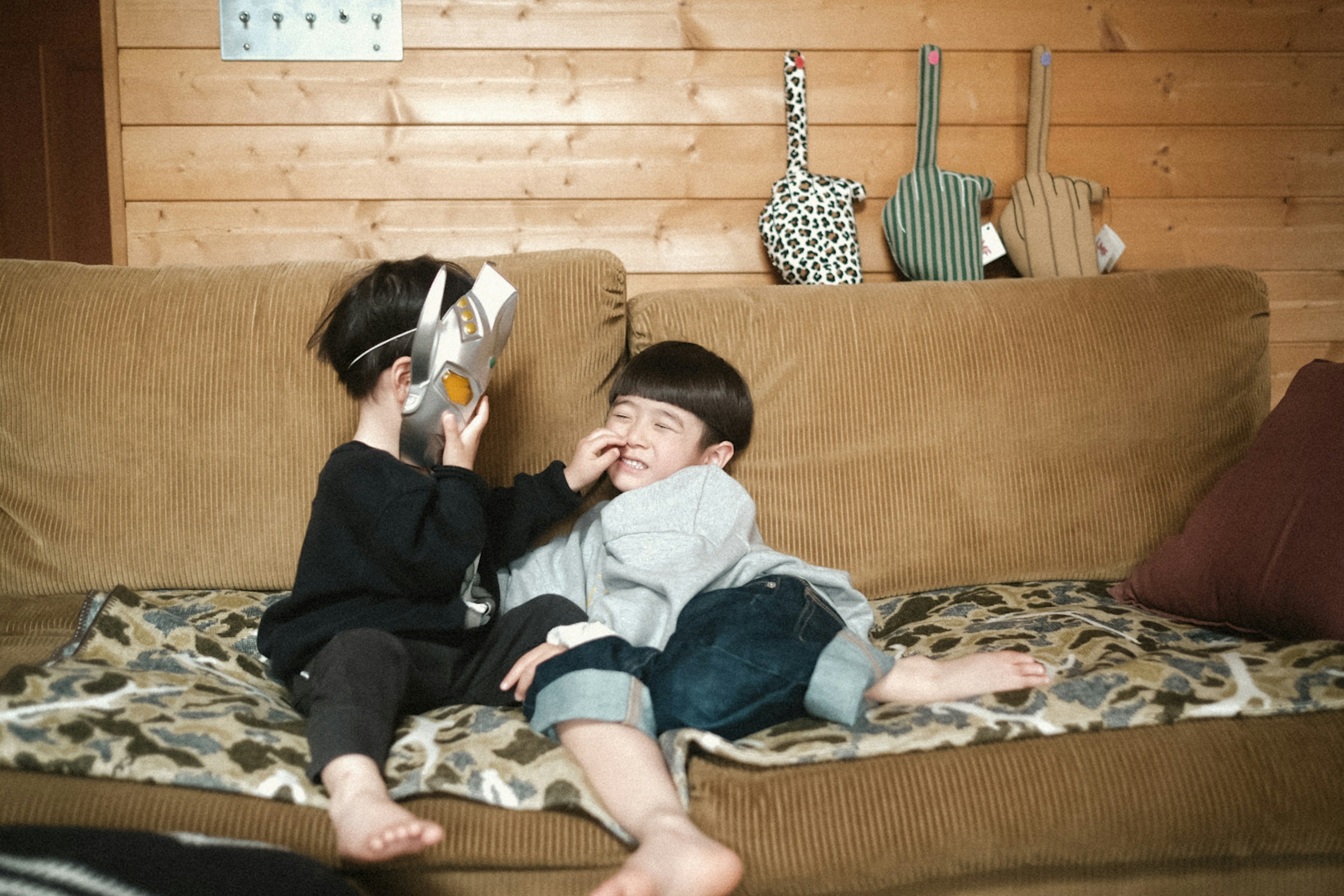 Zwei Kinder sitzen auf einer Couch Eines hält ein Buch während das andere lacht Holzwand und Kissen im Hintergrund