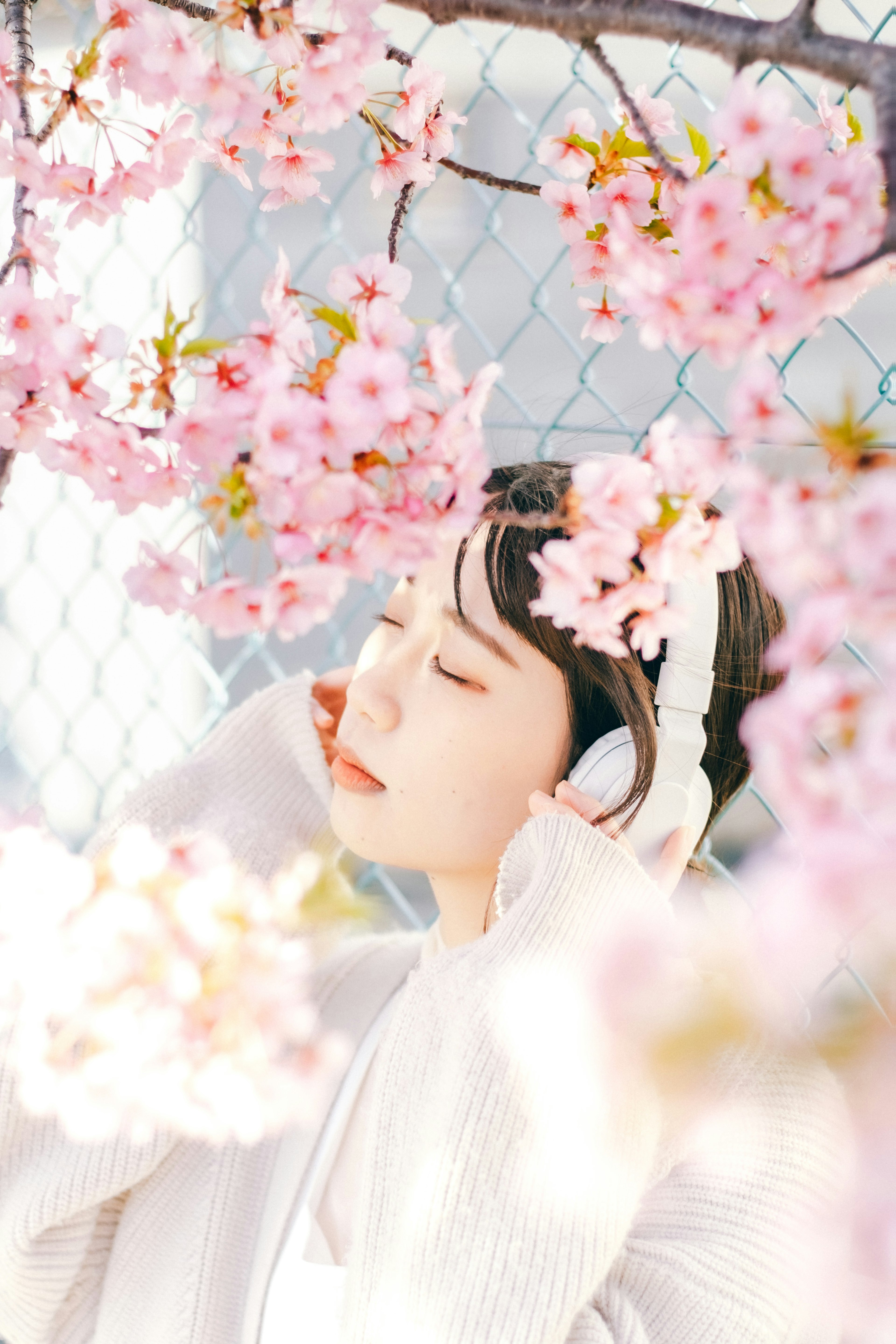 Una mujer con auriculares y los ojos cerrados rodeada de flores de cerezo