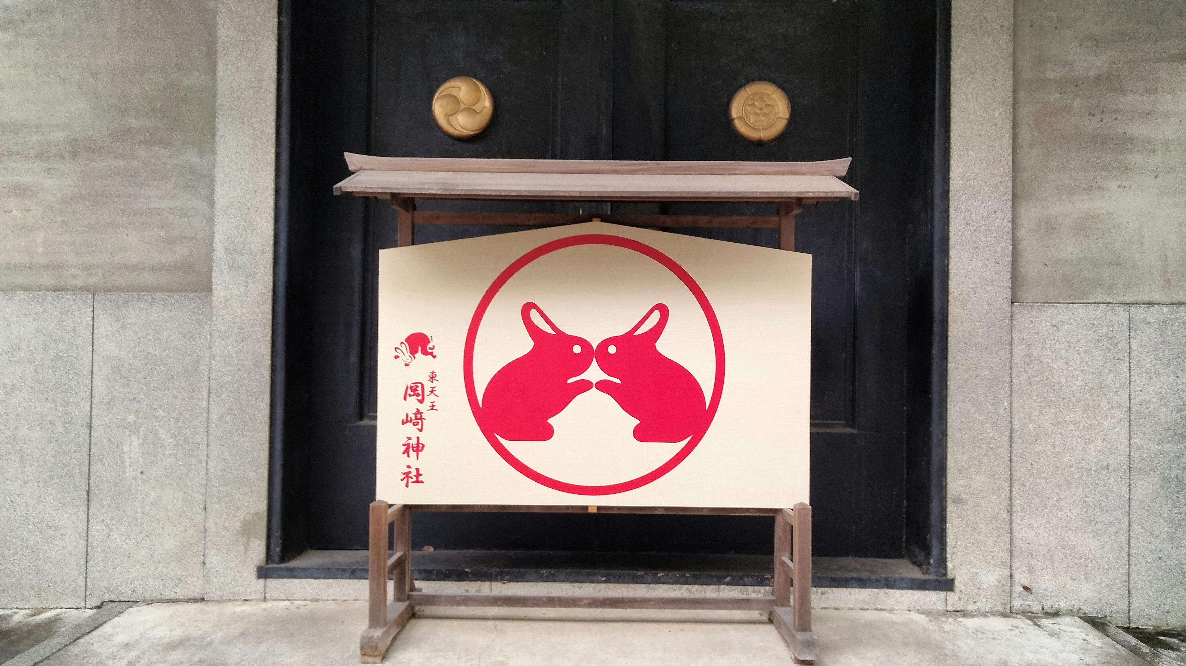 A sign with red rabbits depicted in front of black doors