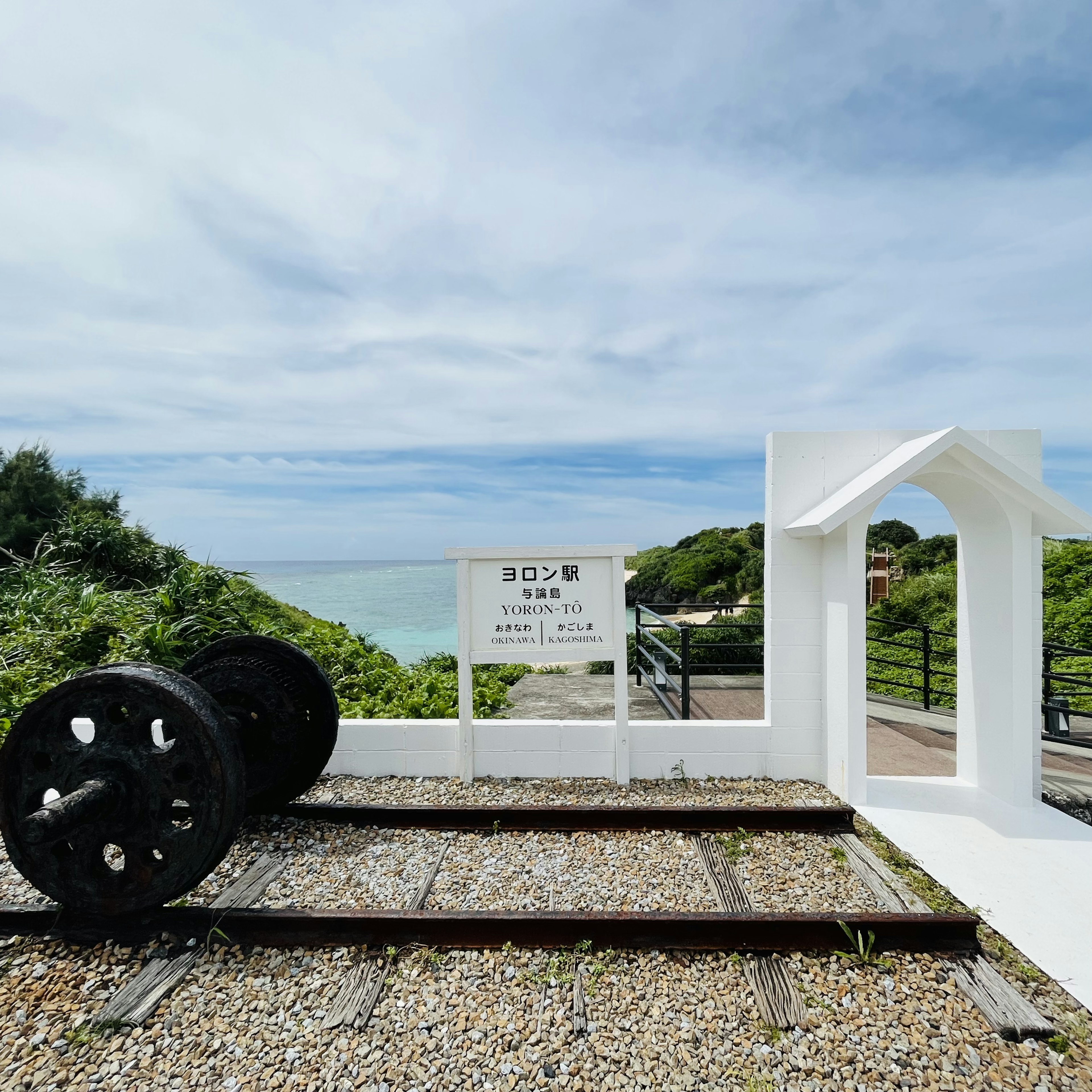 海を背景にした白い構造物と黒い車輪が並ぶレール