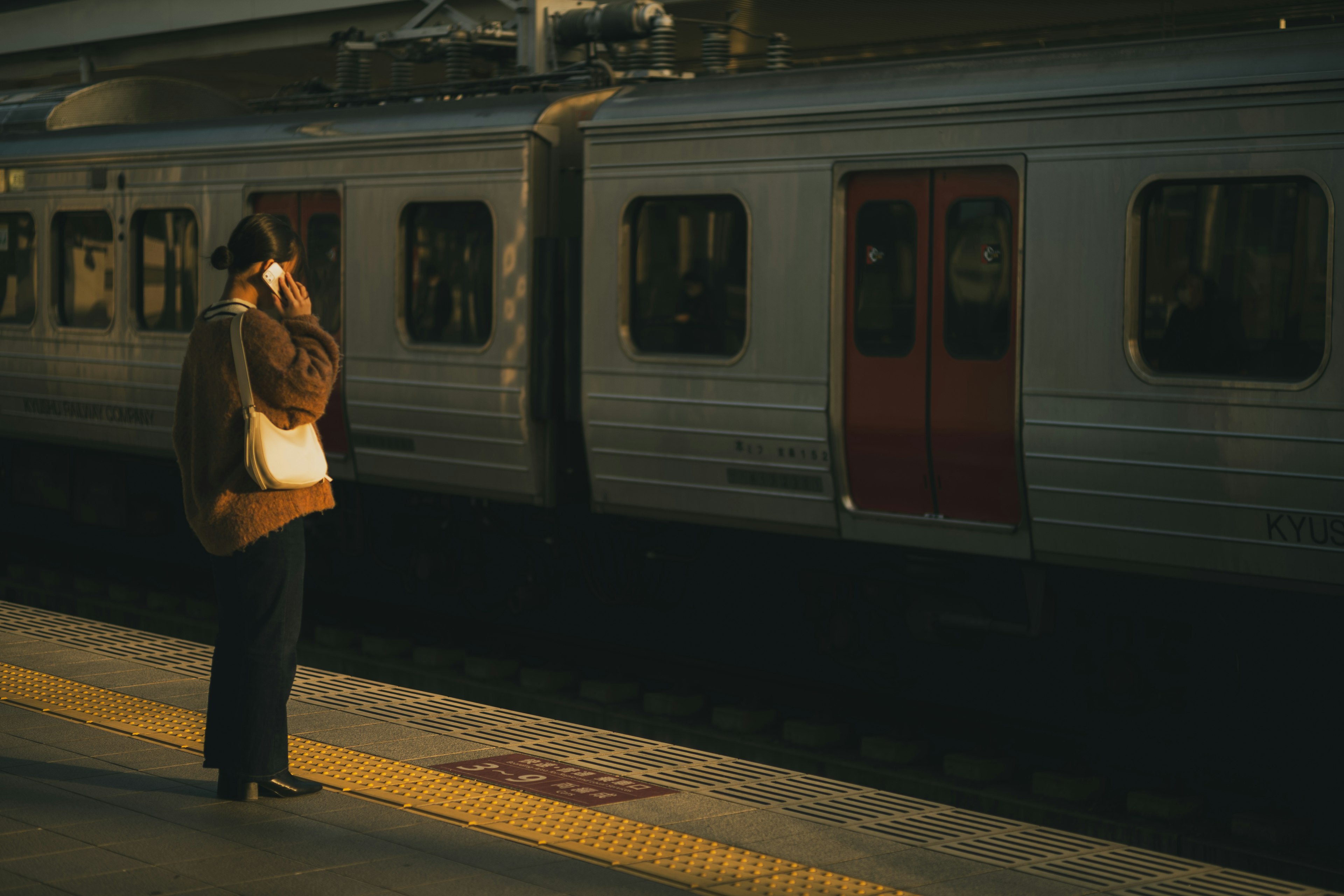 Femme attendant à la gare vêtue de vêtements aux couleurs chaudes train garé à proximité