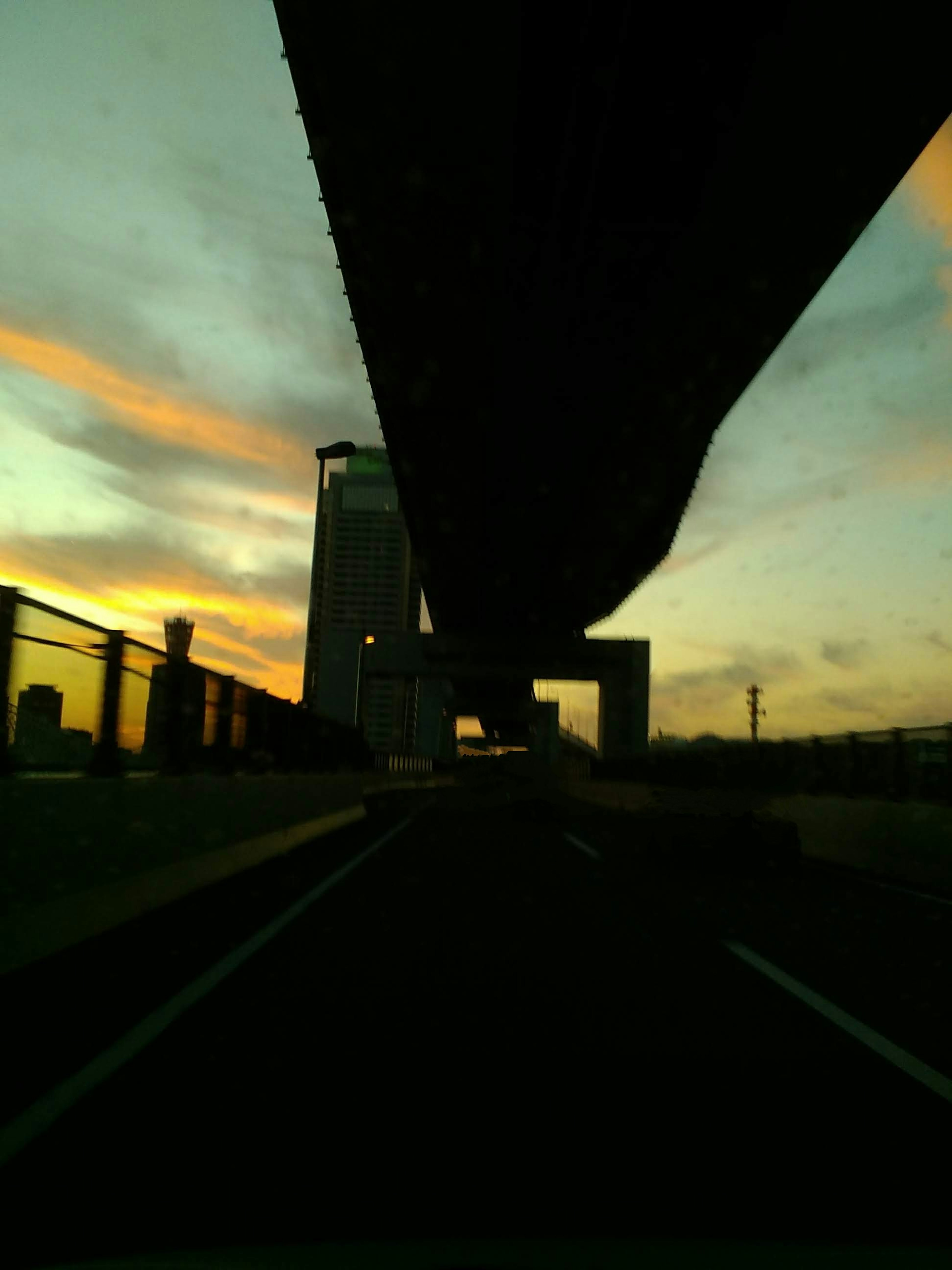 Silhouette einer erhöhten Straße und eines Gebäudes vor einem Sonnenuntergangshimmel