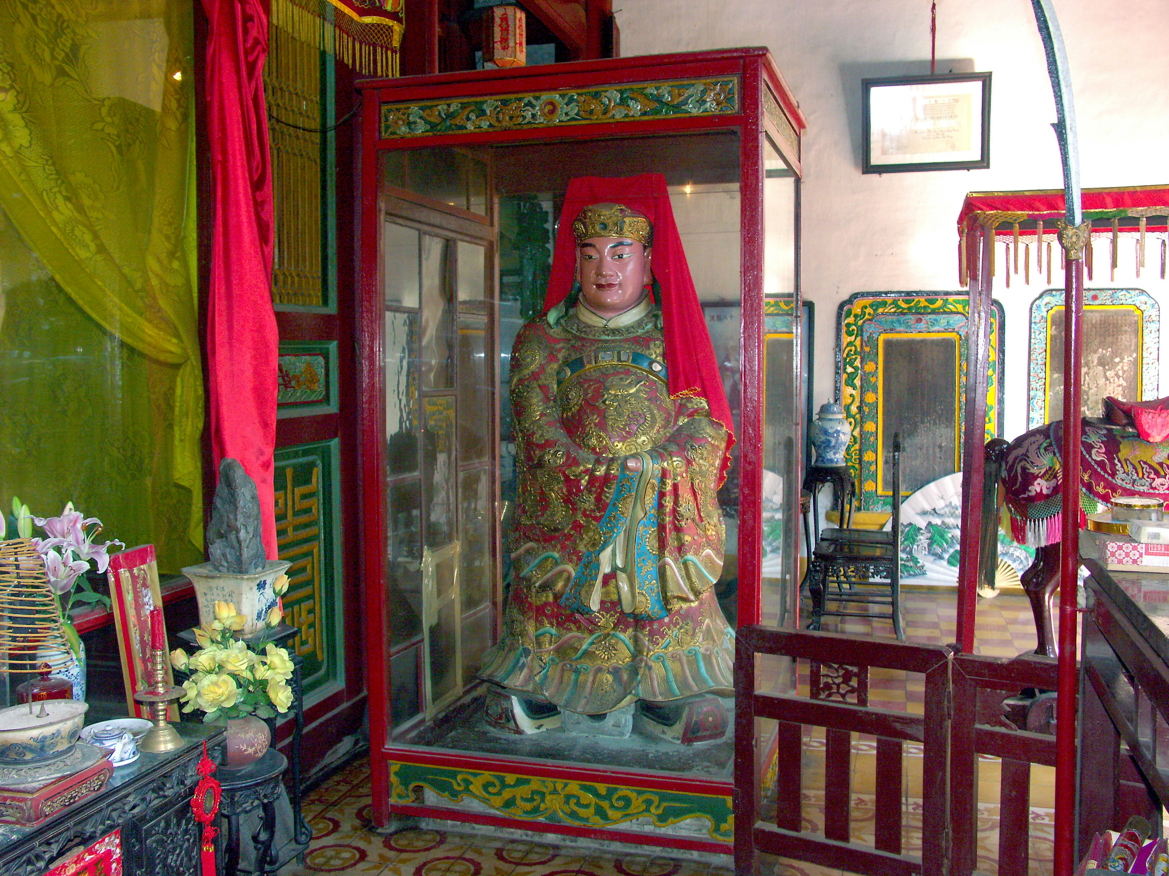 A temple interior featuring a glass case with a statue draped in red fabric