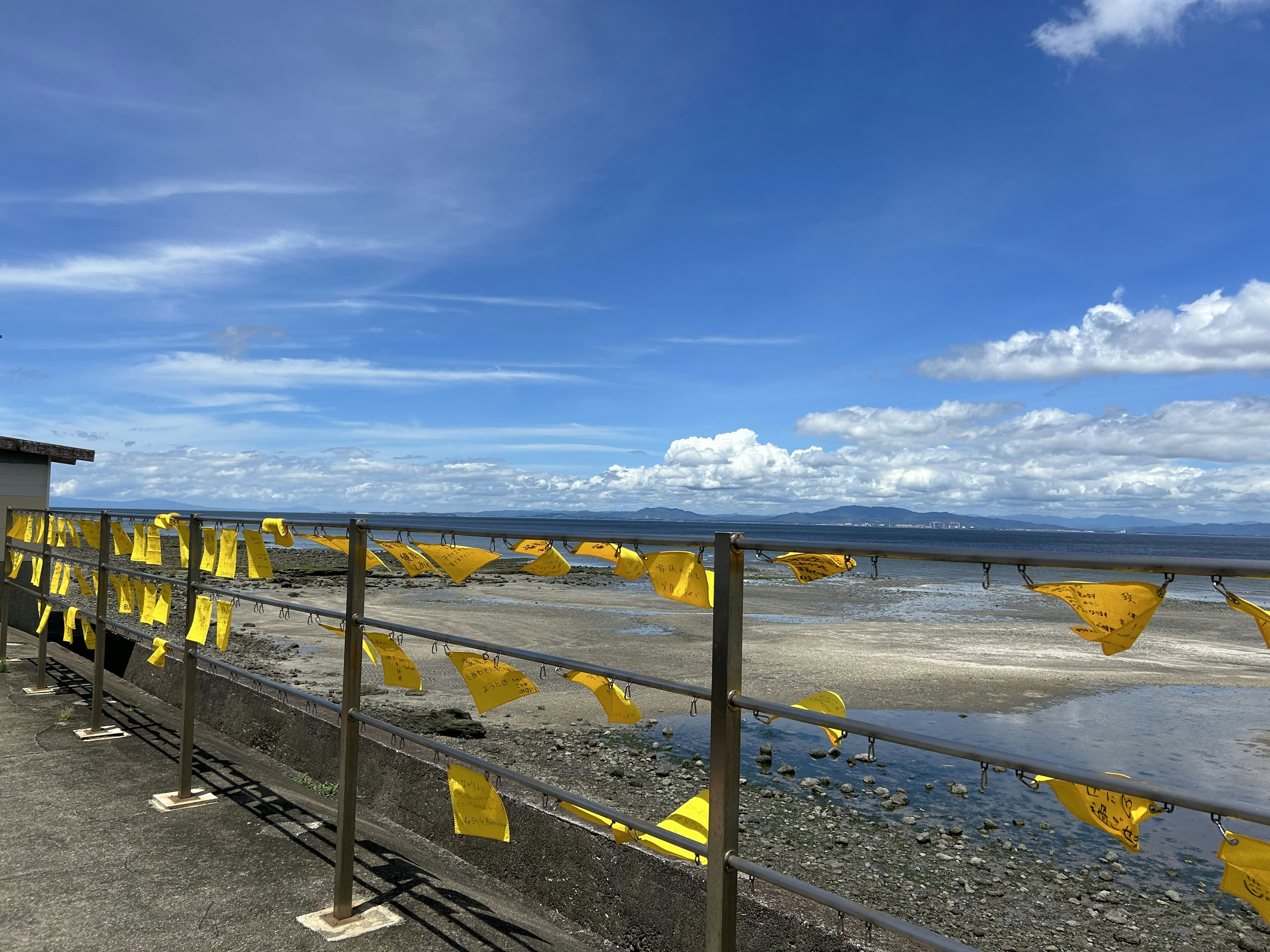 Pemandangan laut di bawah langit biru dengan bendera kuning di pagar