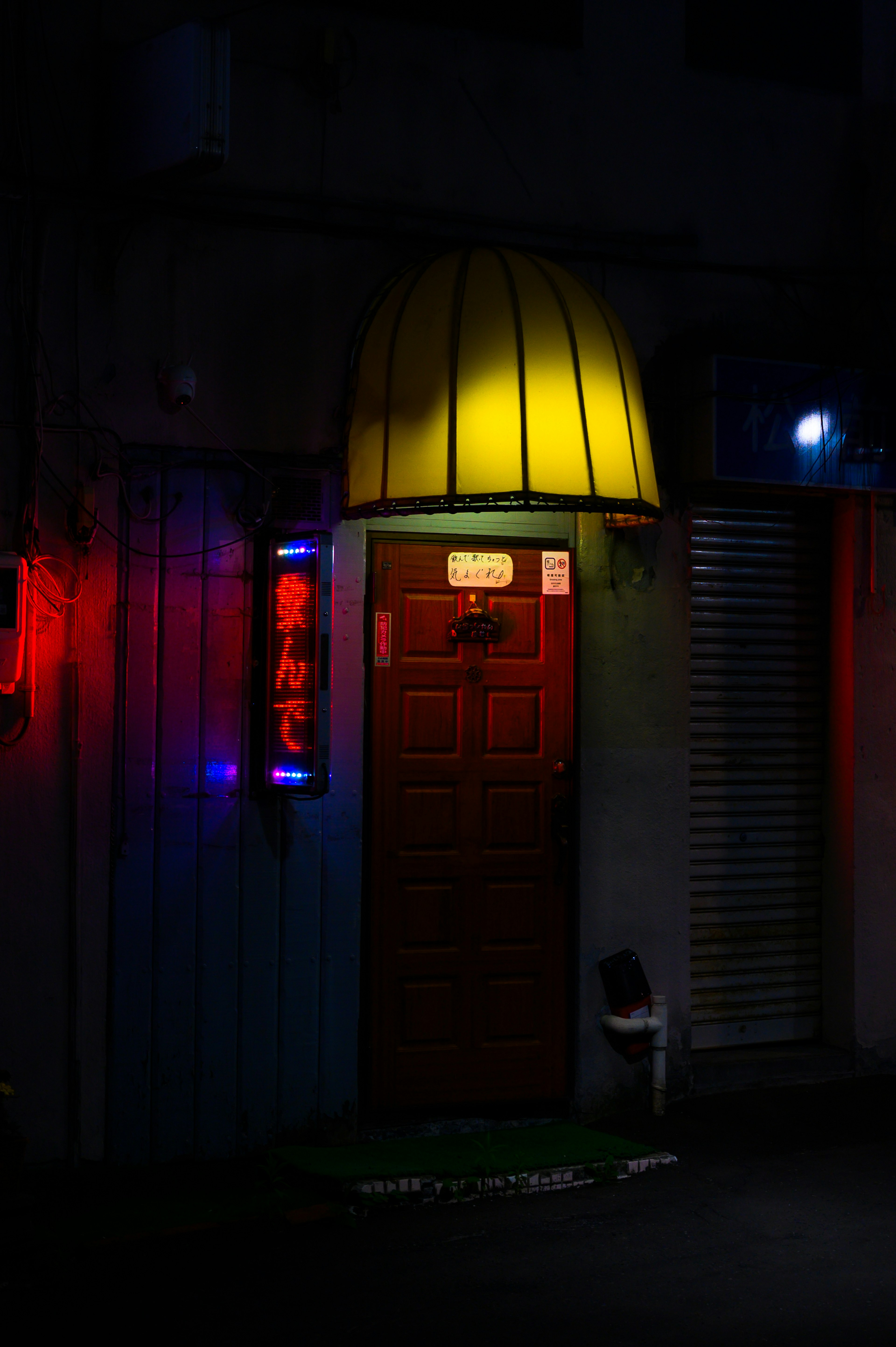 Una porta con un awning giallo illuminata da luci al neon in una strada buia