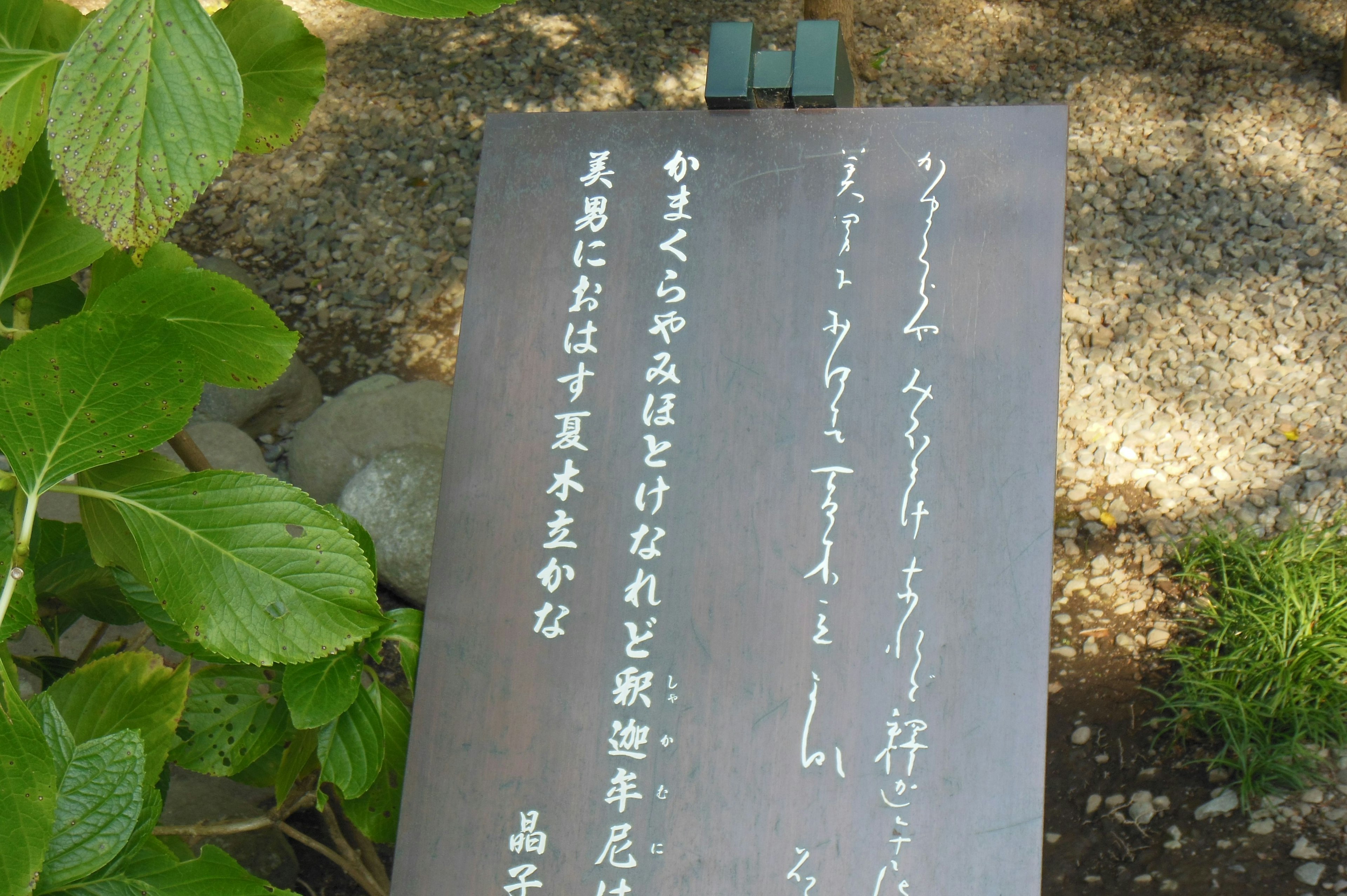 A stone plaque surrounded by green plants featuring Japanese poetry