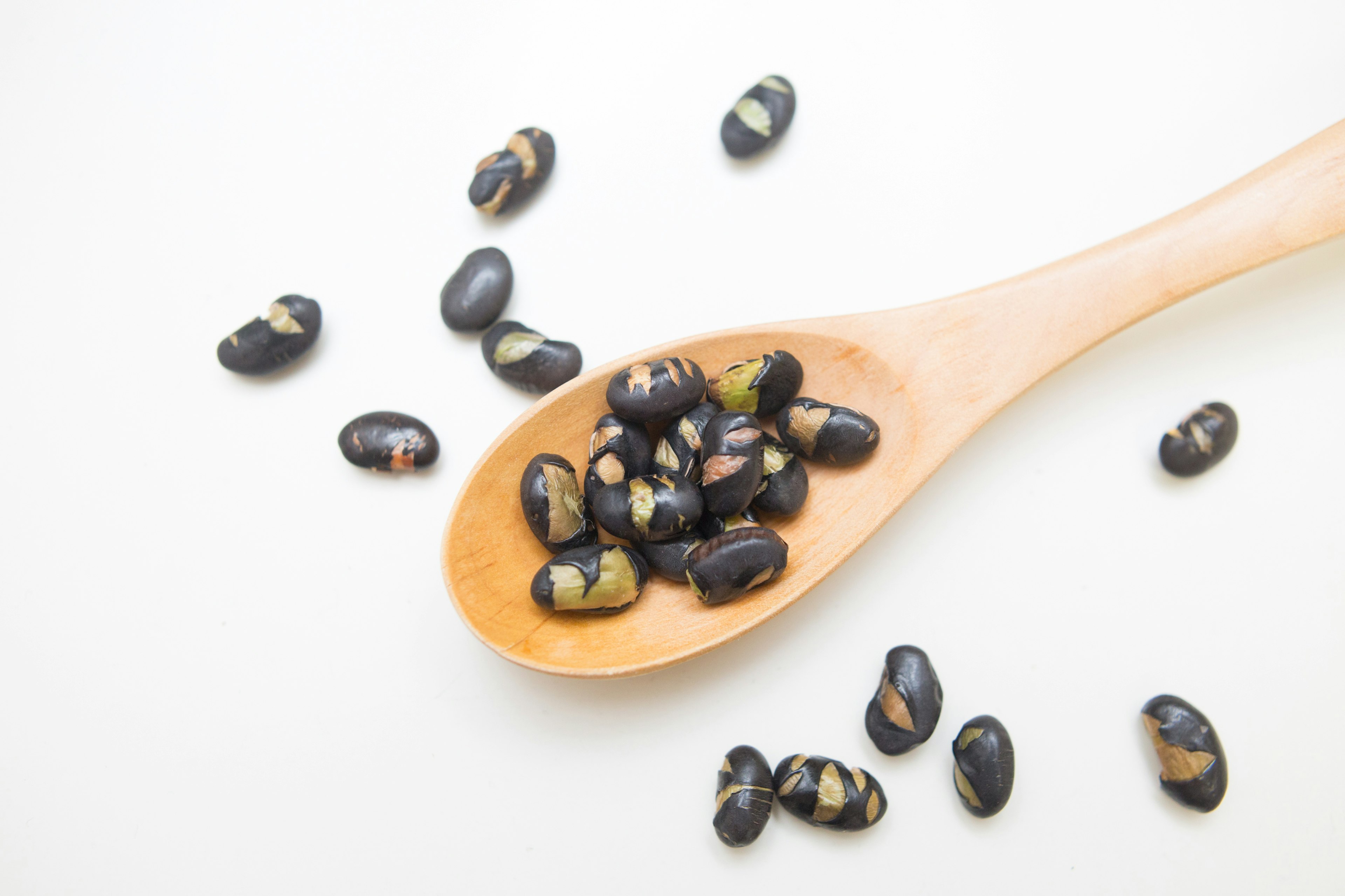 Una cuchara de madera llena de una mezcla de frijoles negros y frijoles verdes