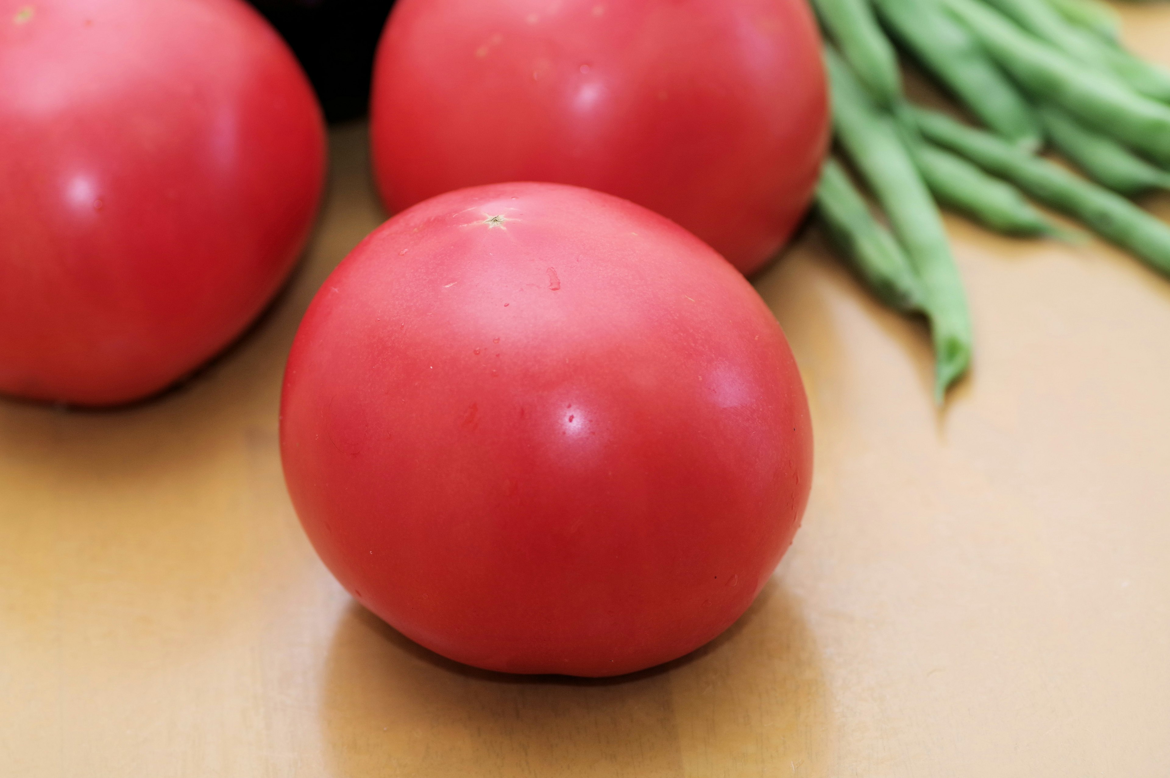 Red tomatoes and green beans on a wooden surface