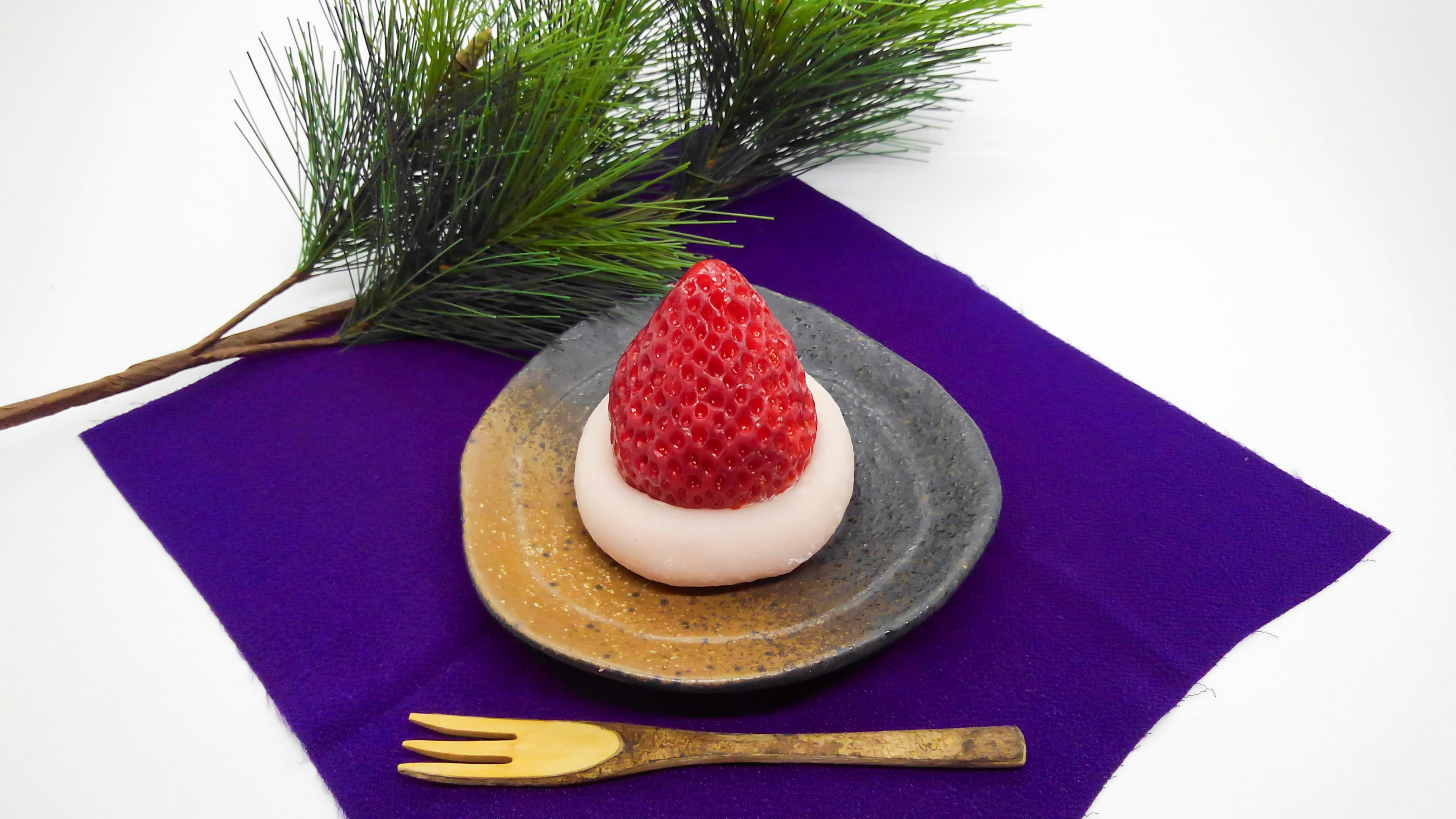 A traditional Japanese dessert topped with a red strawberry on a small plate placed on a purple cloth