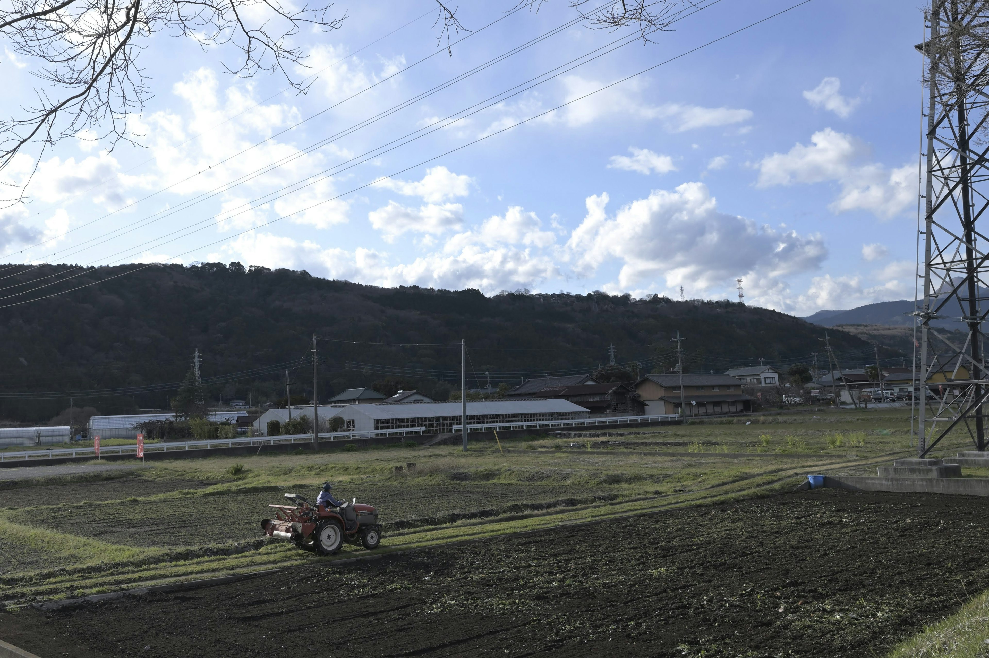 农业拖拉机在广阔的田野中工作，蓝天和山脉在背景中