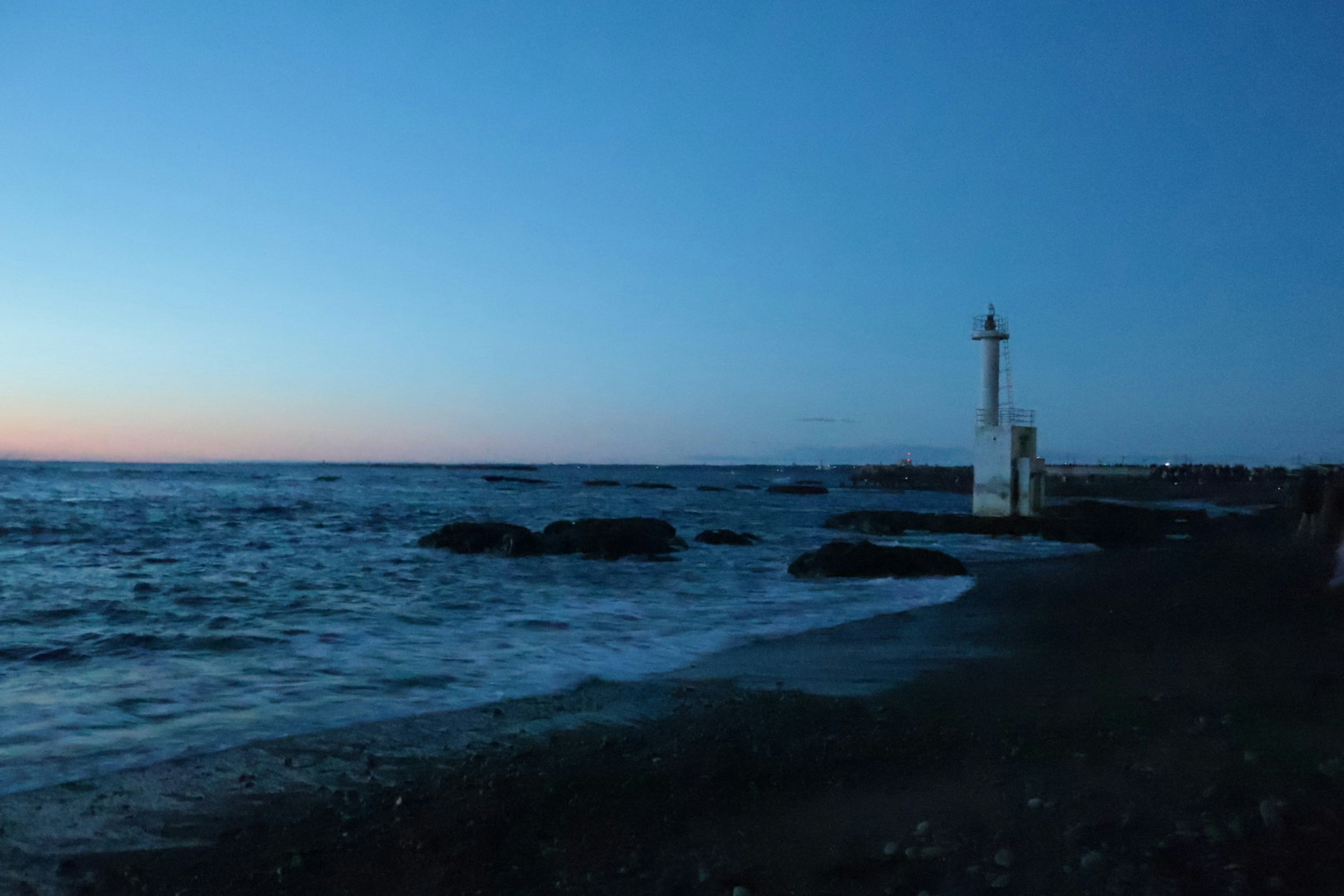 Coastal scene at dusk featuring a lighthouse and rocky shoreline