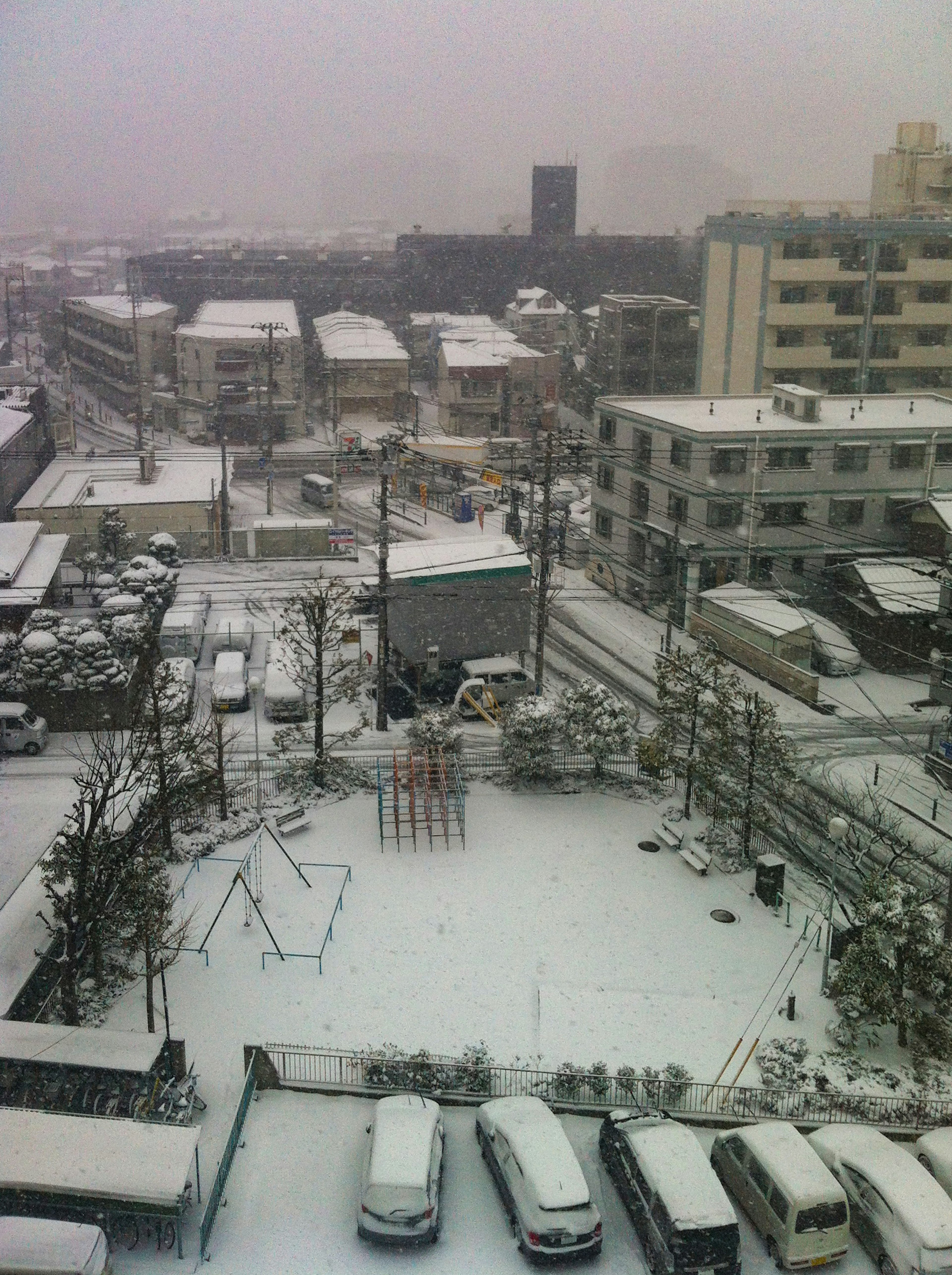 Snow-covered urban landscape with visible parking lot and playground equipment