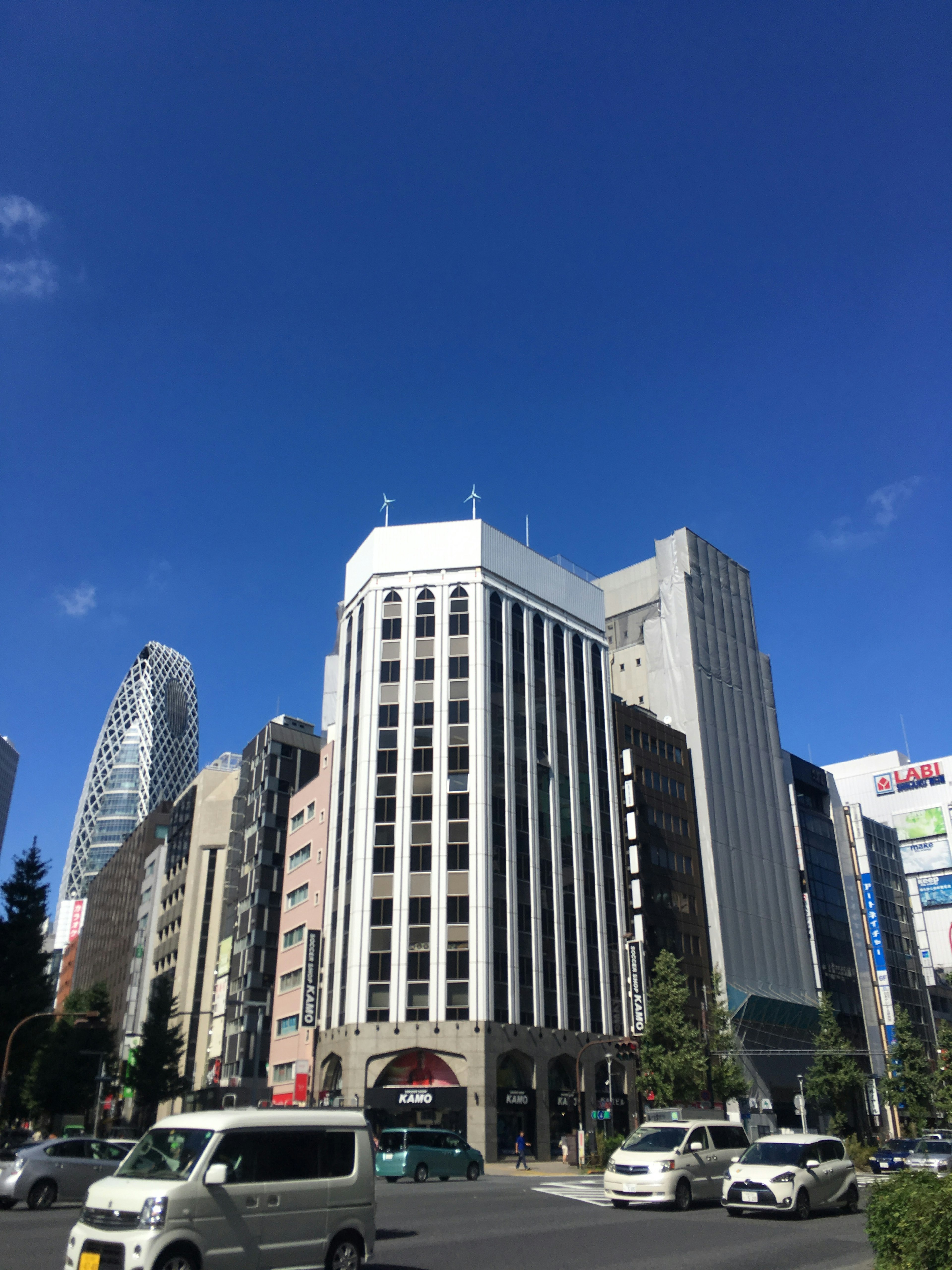 Bangunan dengan eksterior putih dan garis hitam di bawah langit biru cerah dikelilingi oleh gedung pencakar langit lainnya