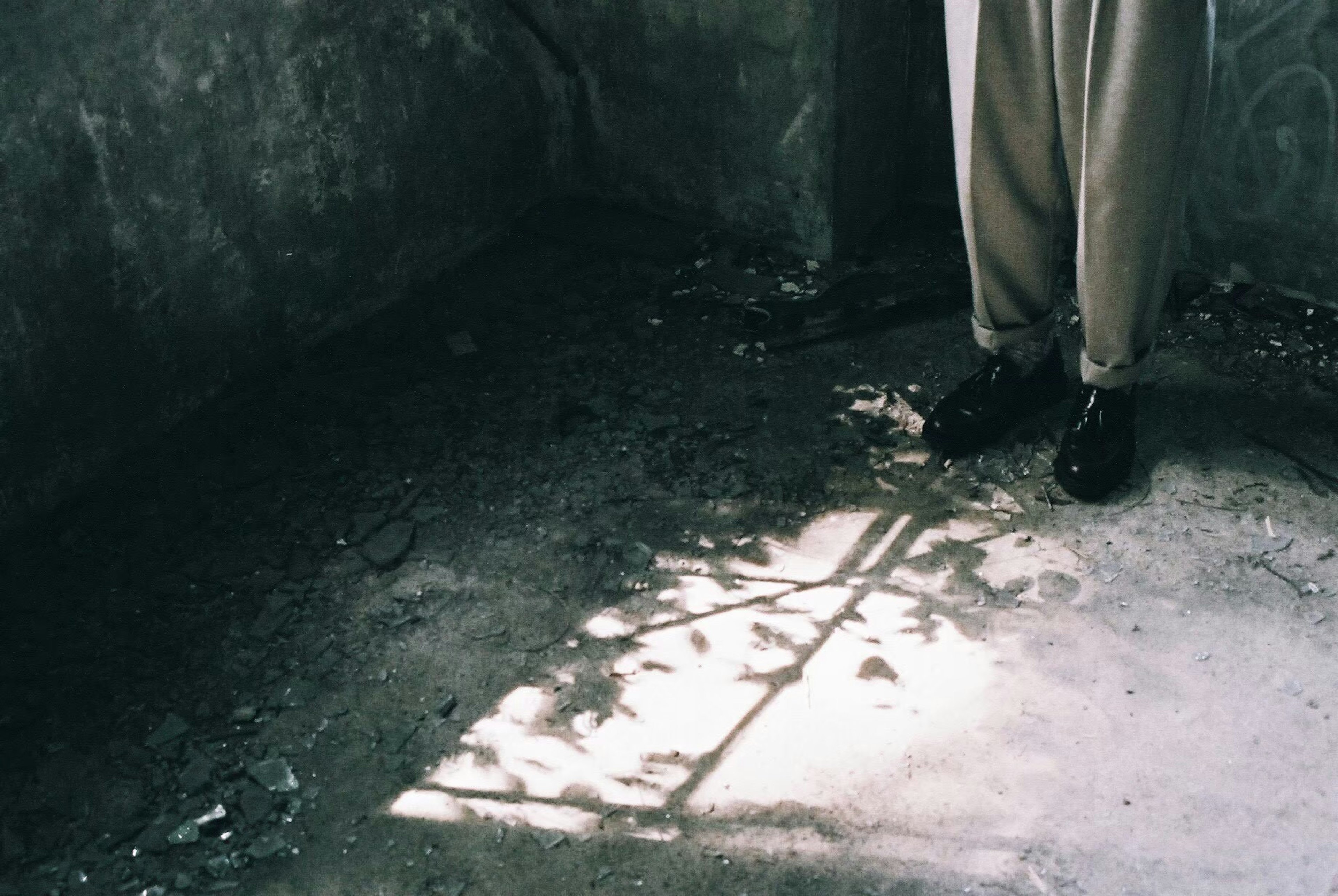 Person's feet standing in a corner of a room with contrasting light and shadow