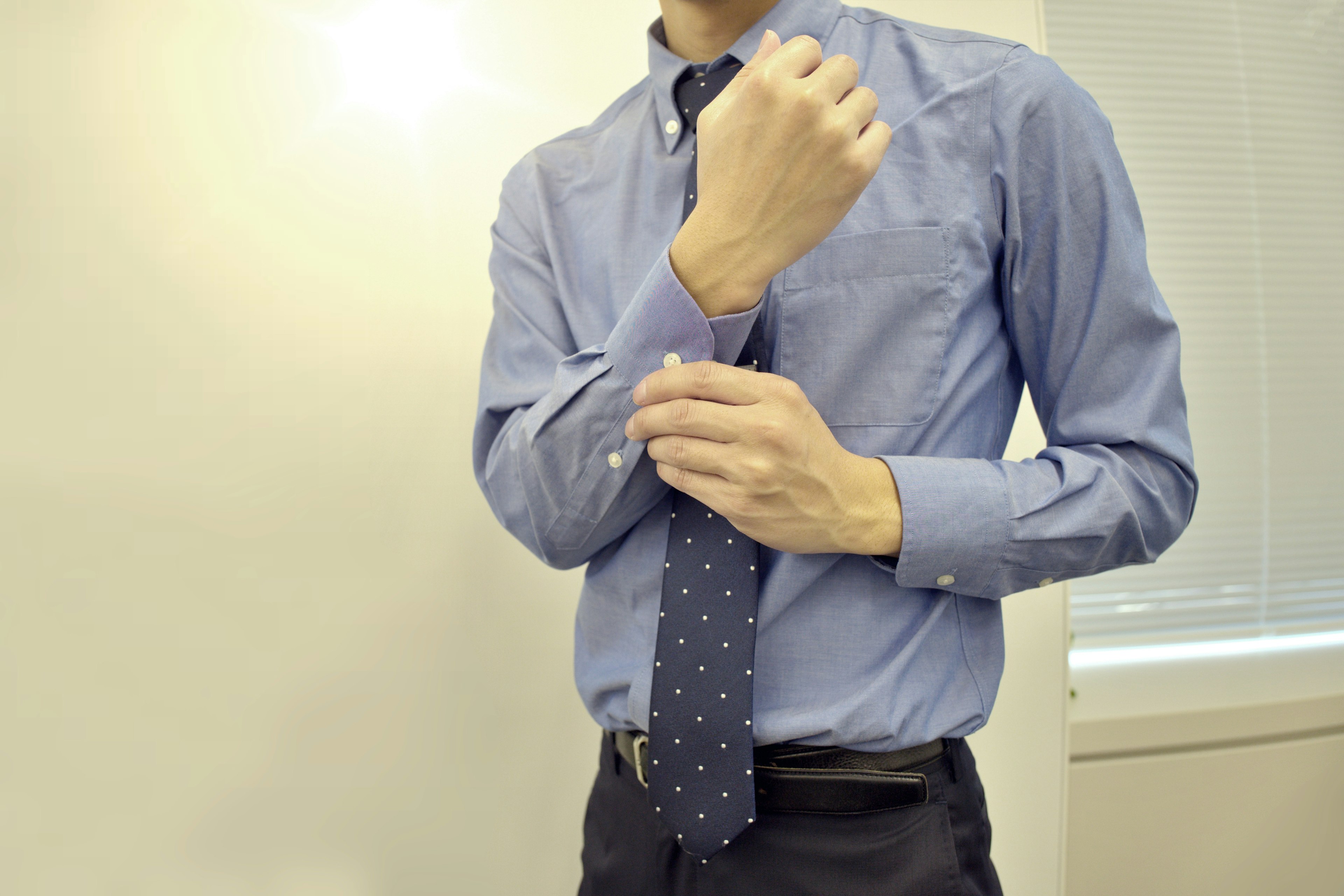 Uomo che regola la sua cravatta indossando una camicia blu