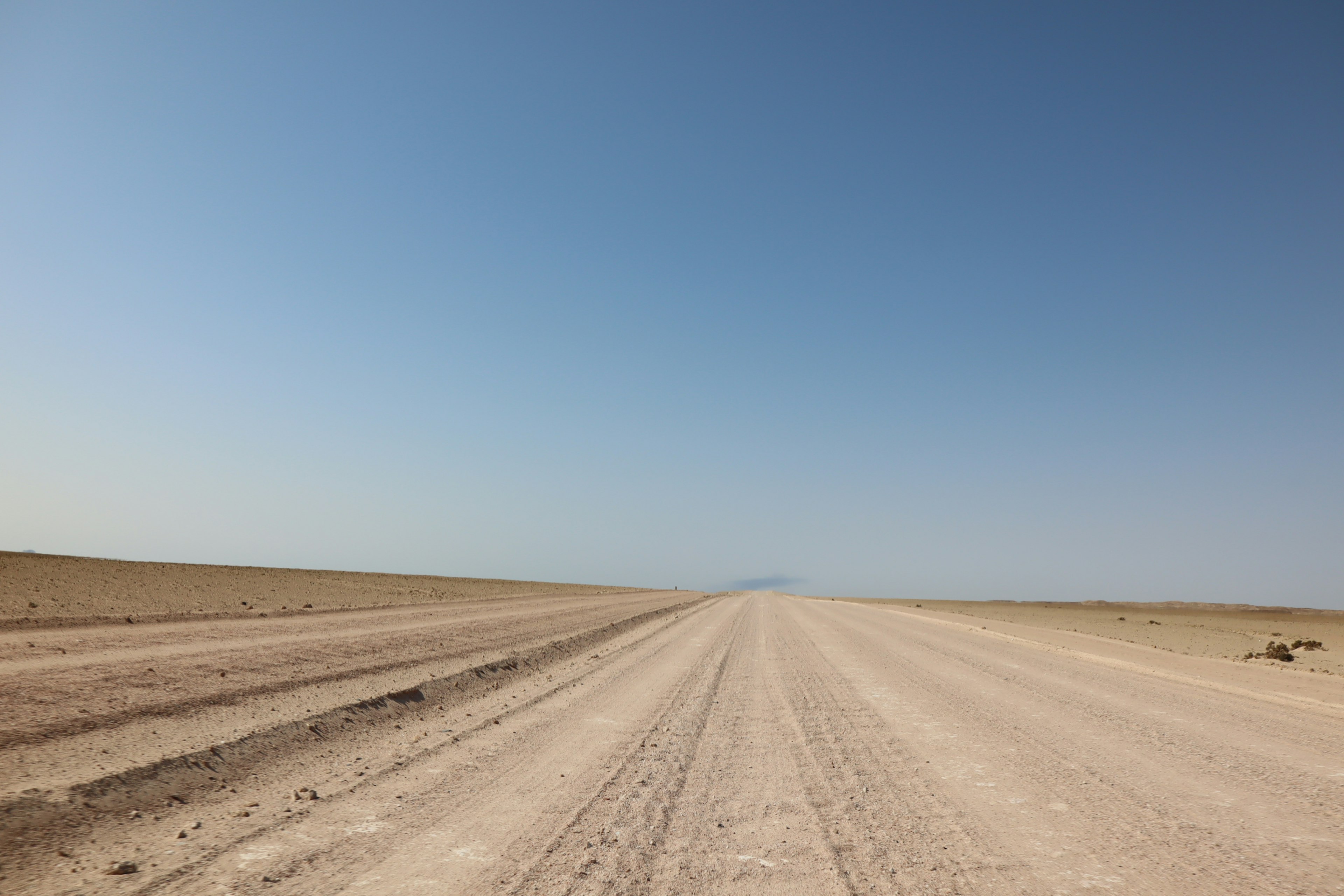 A gravel road stretching across dry land under a clear blue sky