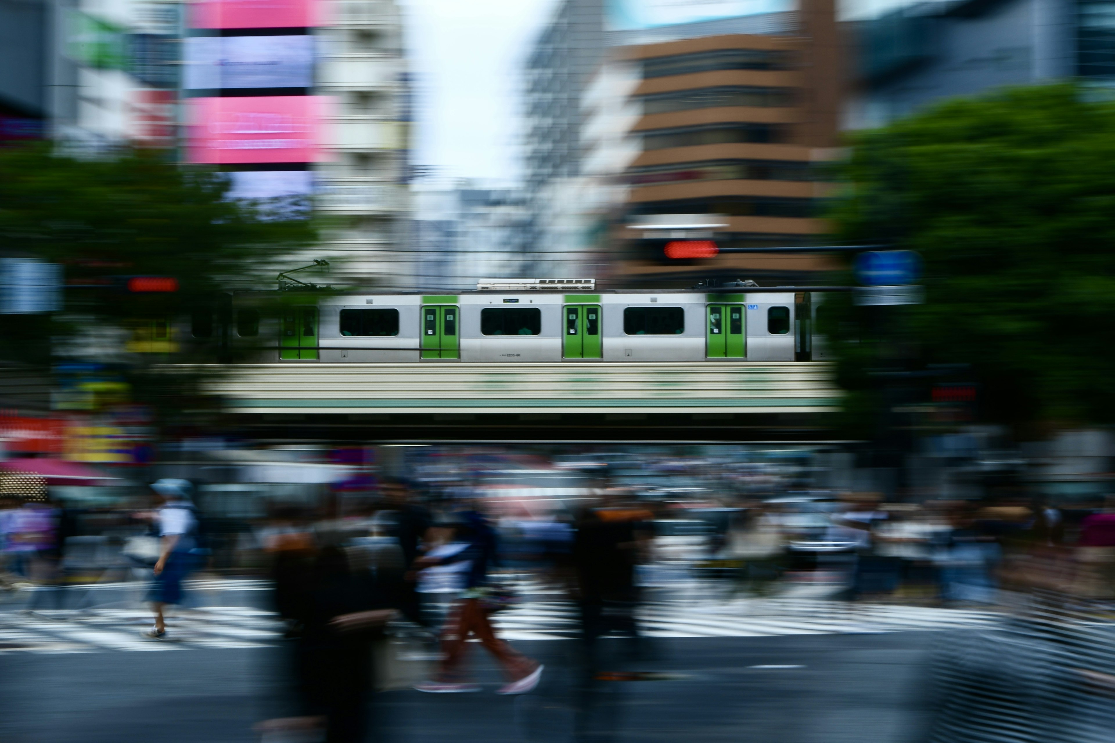 Escena urbana borrosa con un tren verde pasando sobre una intersección concurrida