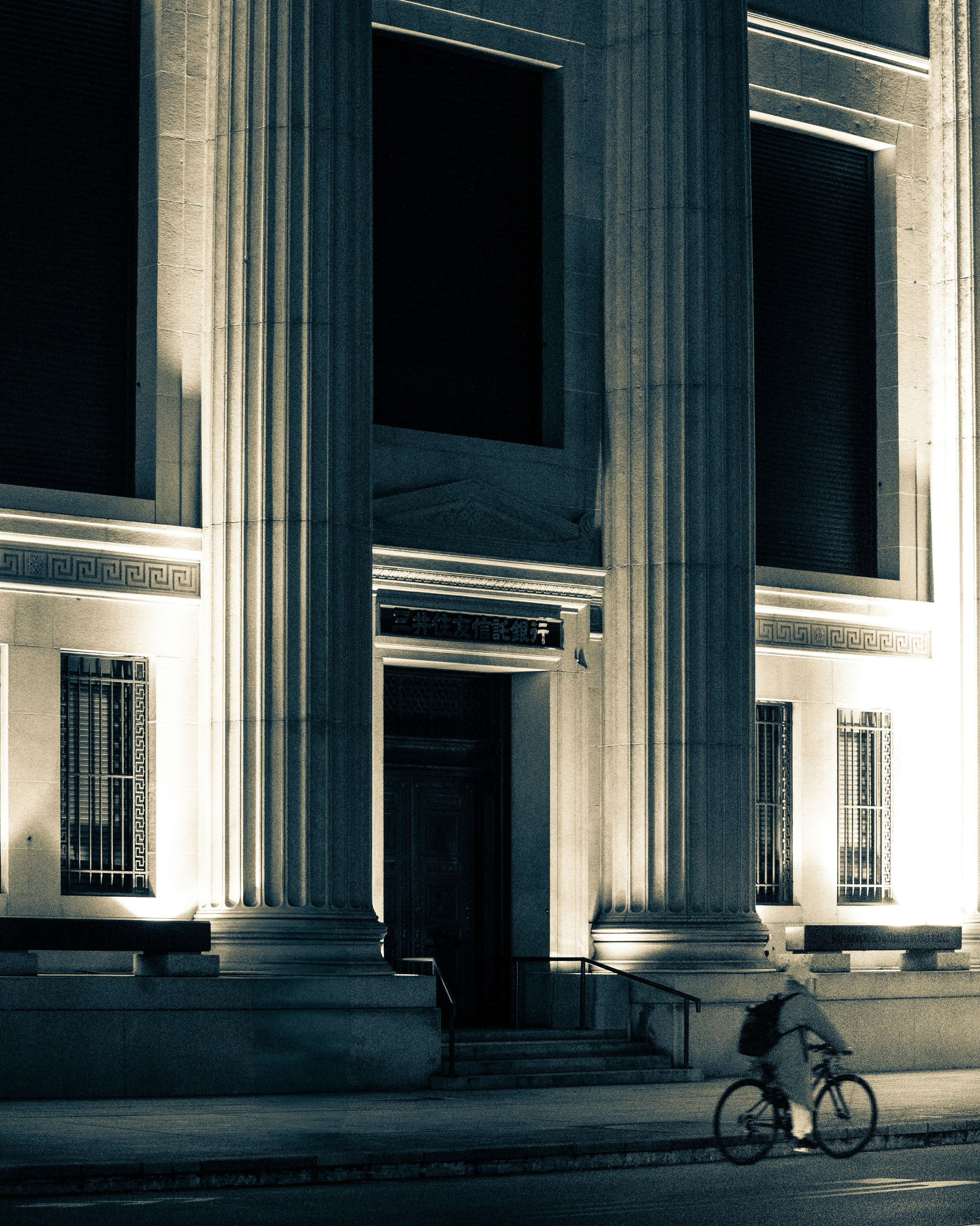 Persona montando en bicicleta frente a un edificio con columnas por la noche