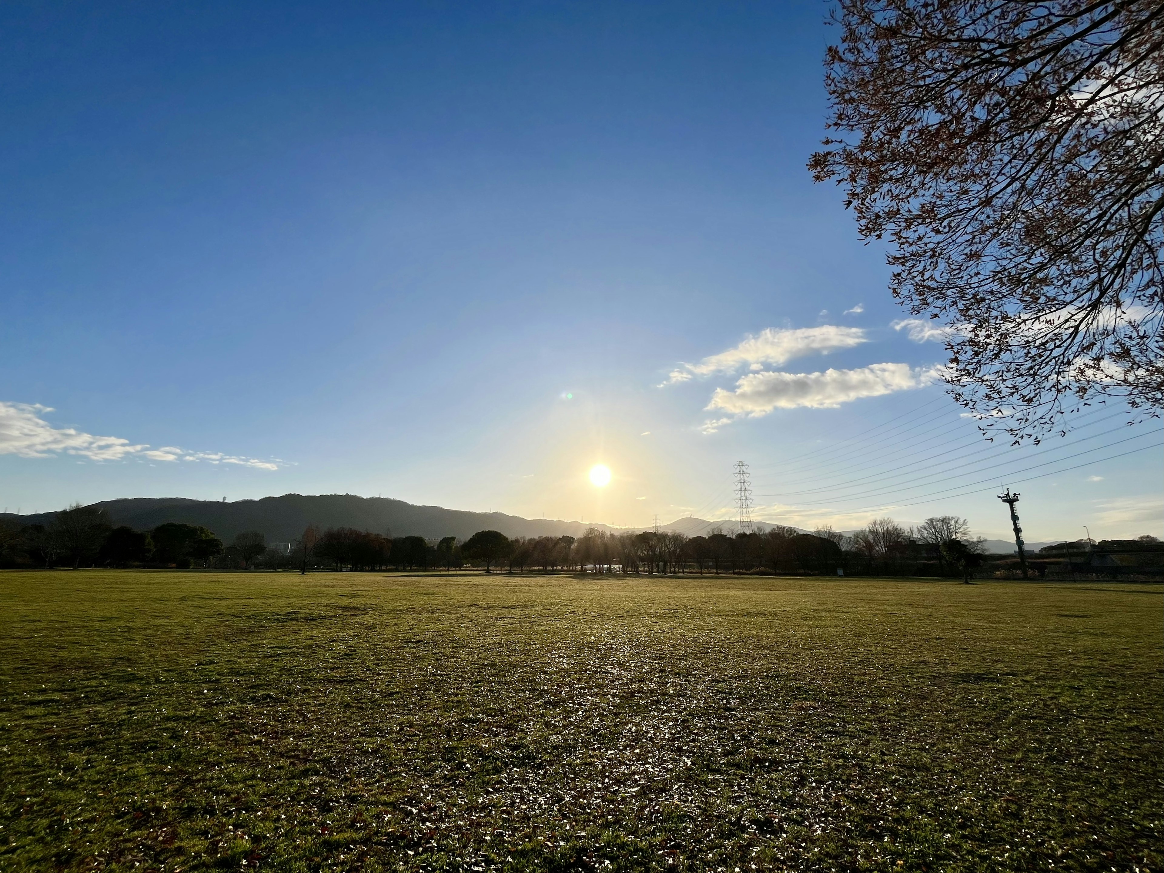 Landschaft mit aufgehender Sonne unter blauem Himmel grünem Feld und Silhouetten von Bergen