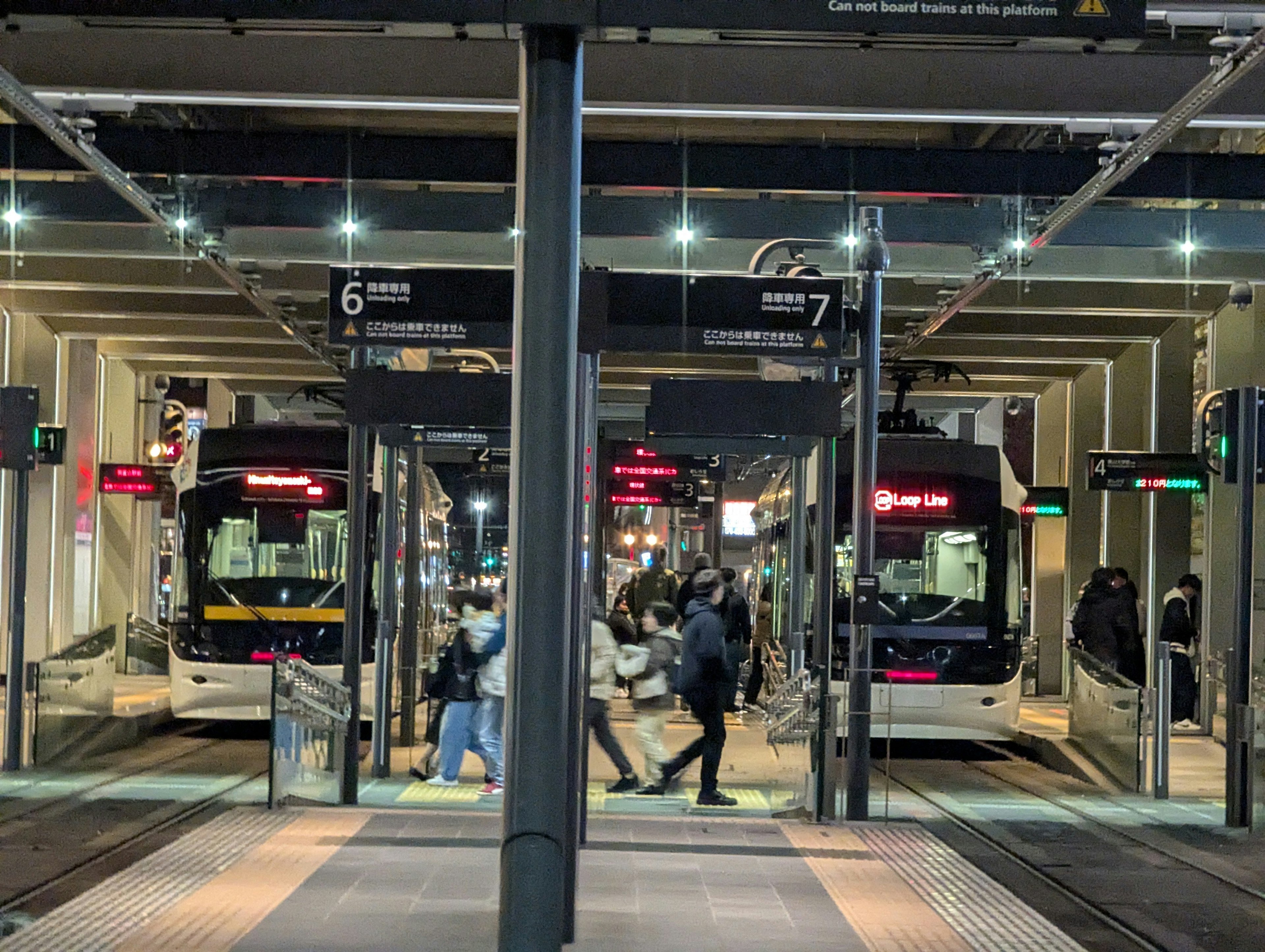 夜間公車站的場景，乘客穿行，兩輛公車停靠