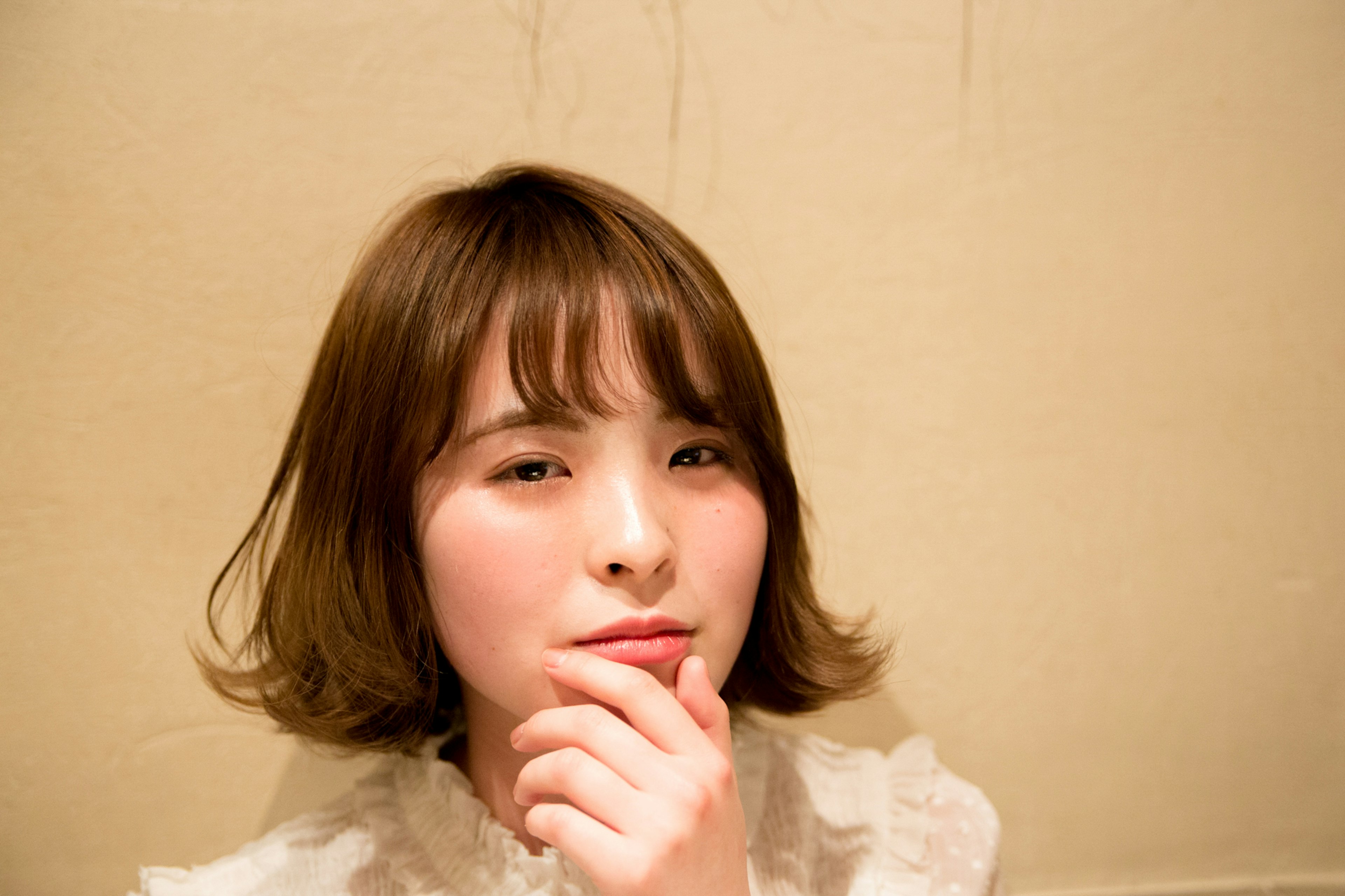 Une femme dans une pose pensive avec des cheveux courts et une frange sur un fond crème