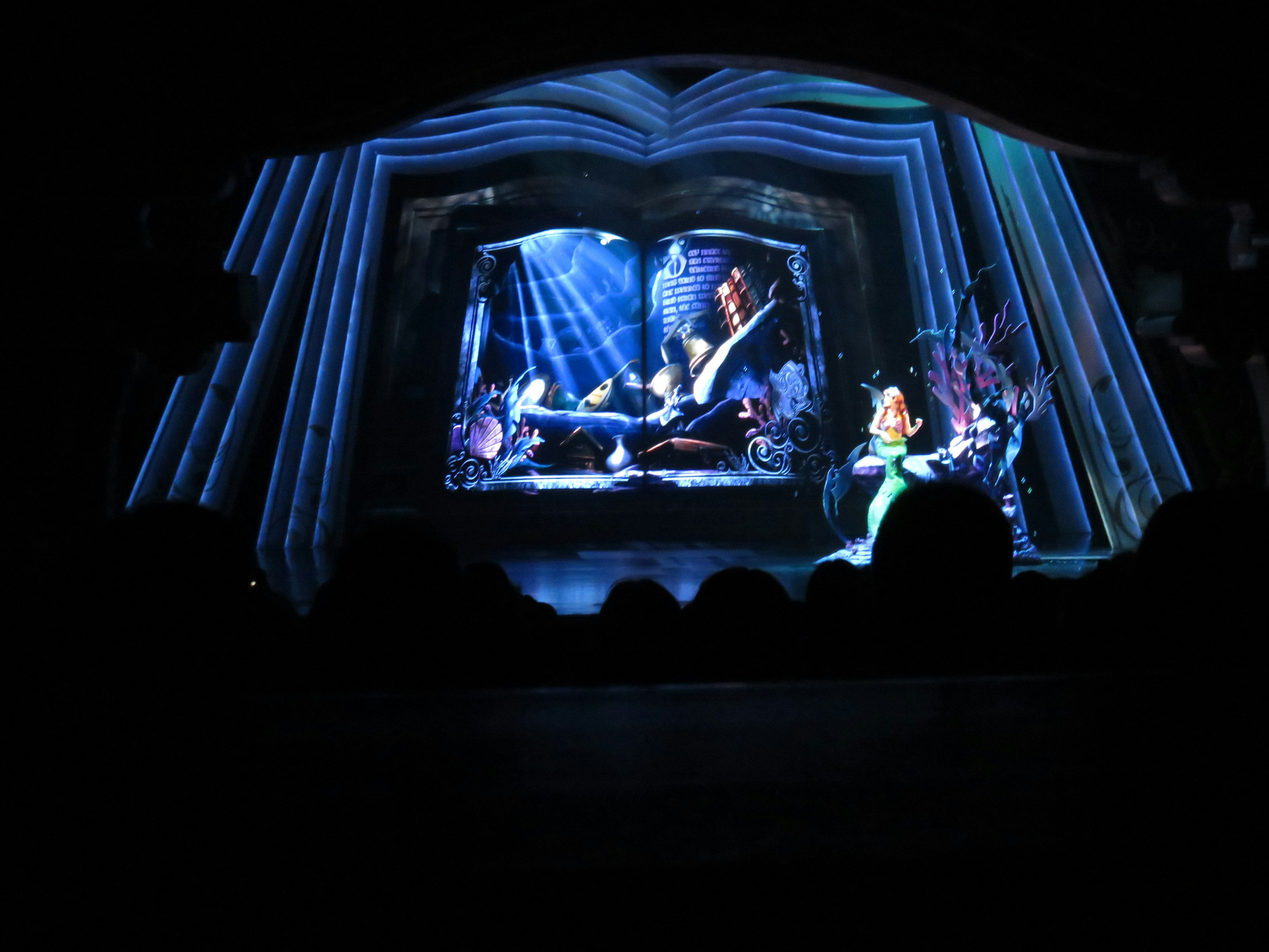 A large book on stage with Ariel sitting in front of it