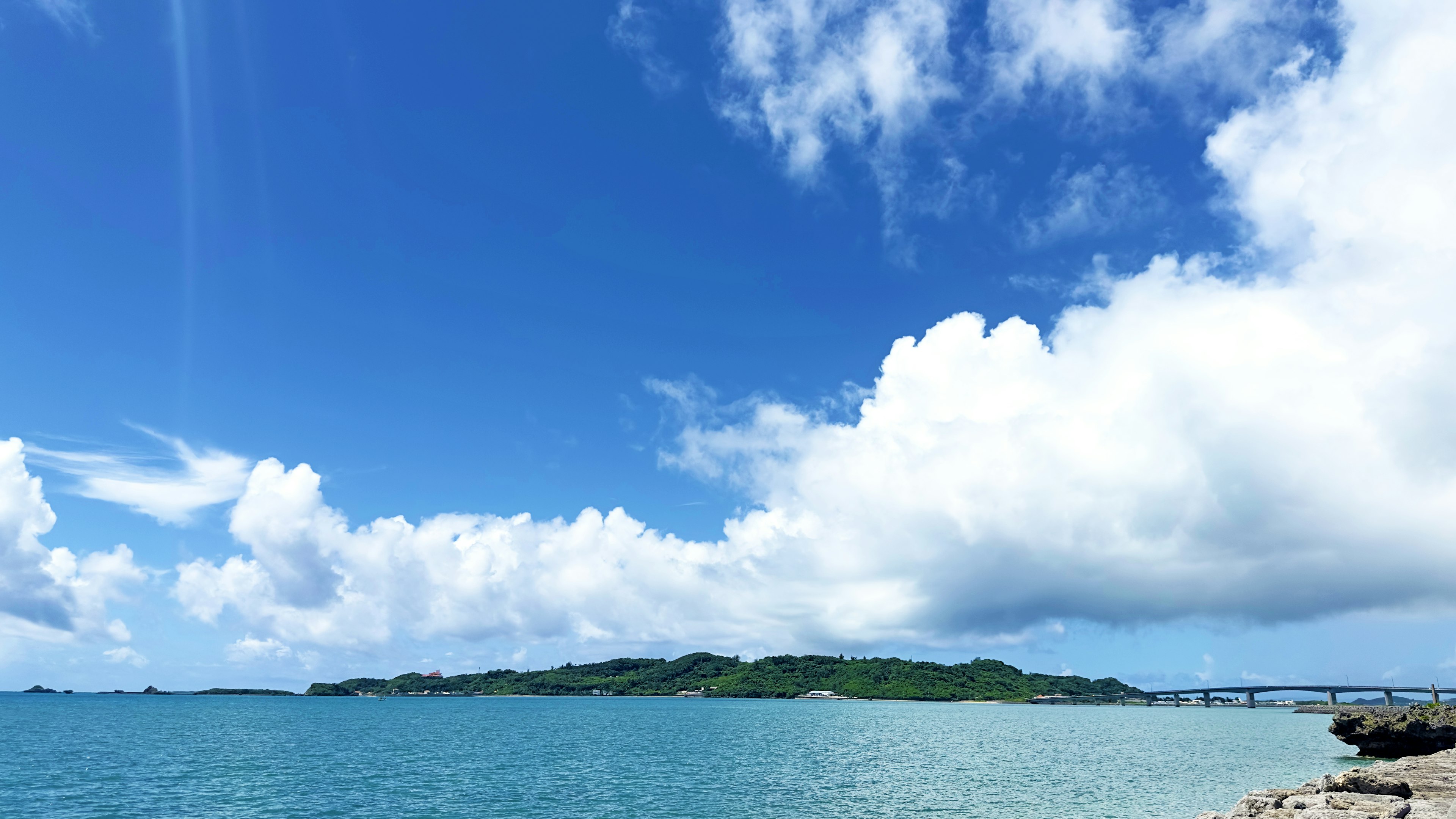 Scenic view of blue sea and white clouds with an island in the background