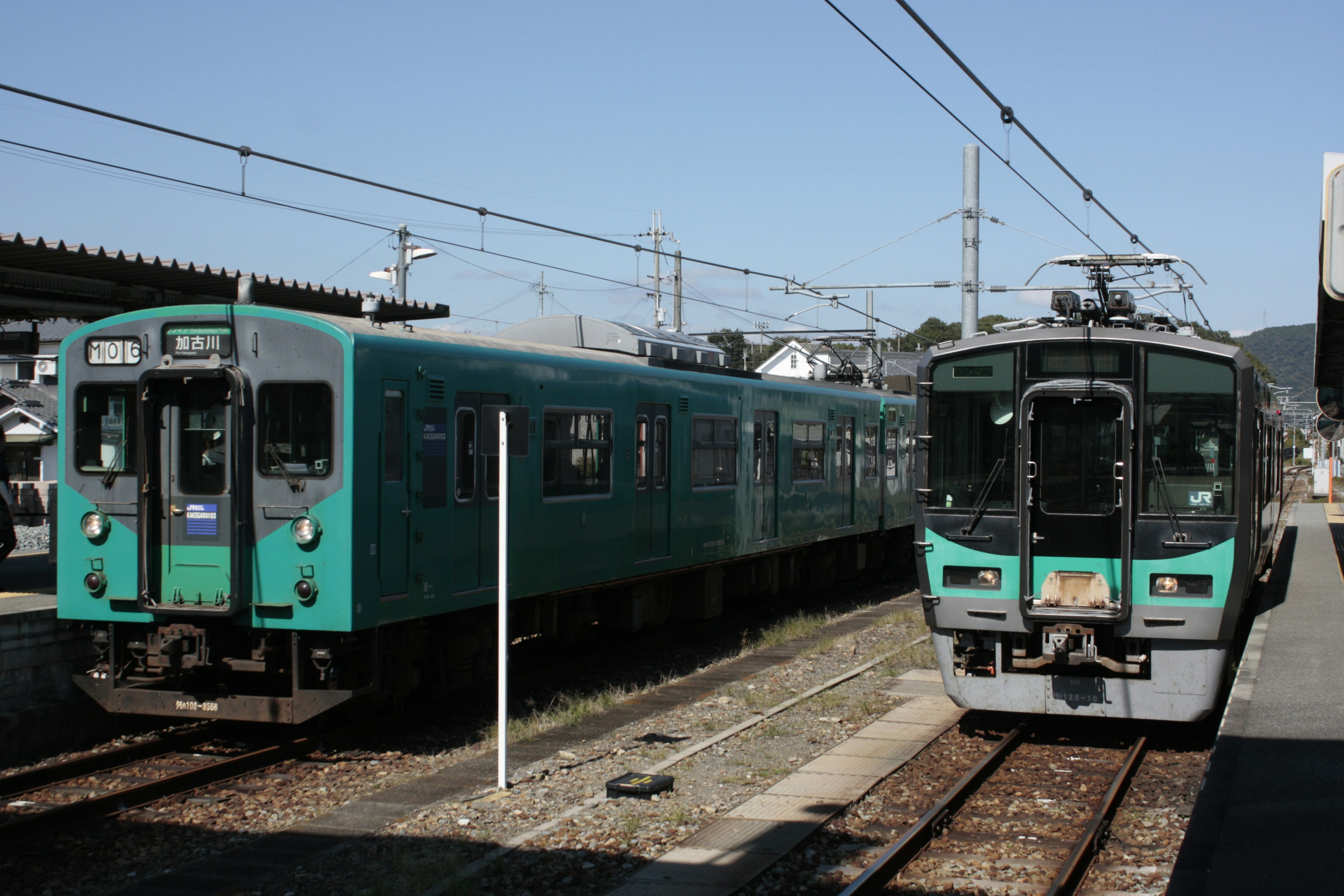 Two trains at a station under a clear blue sky