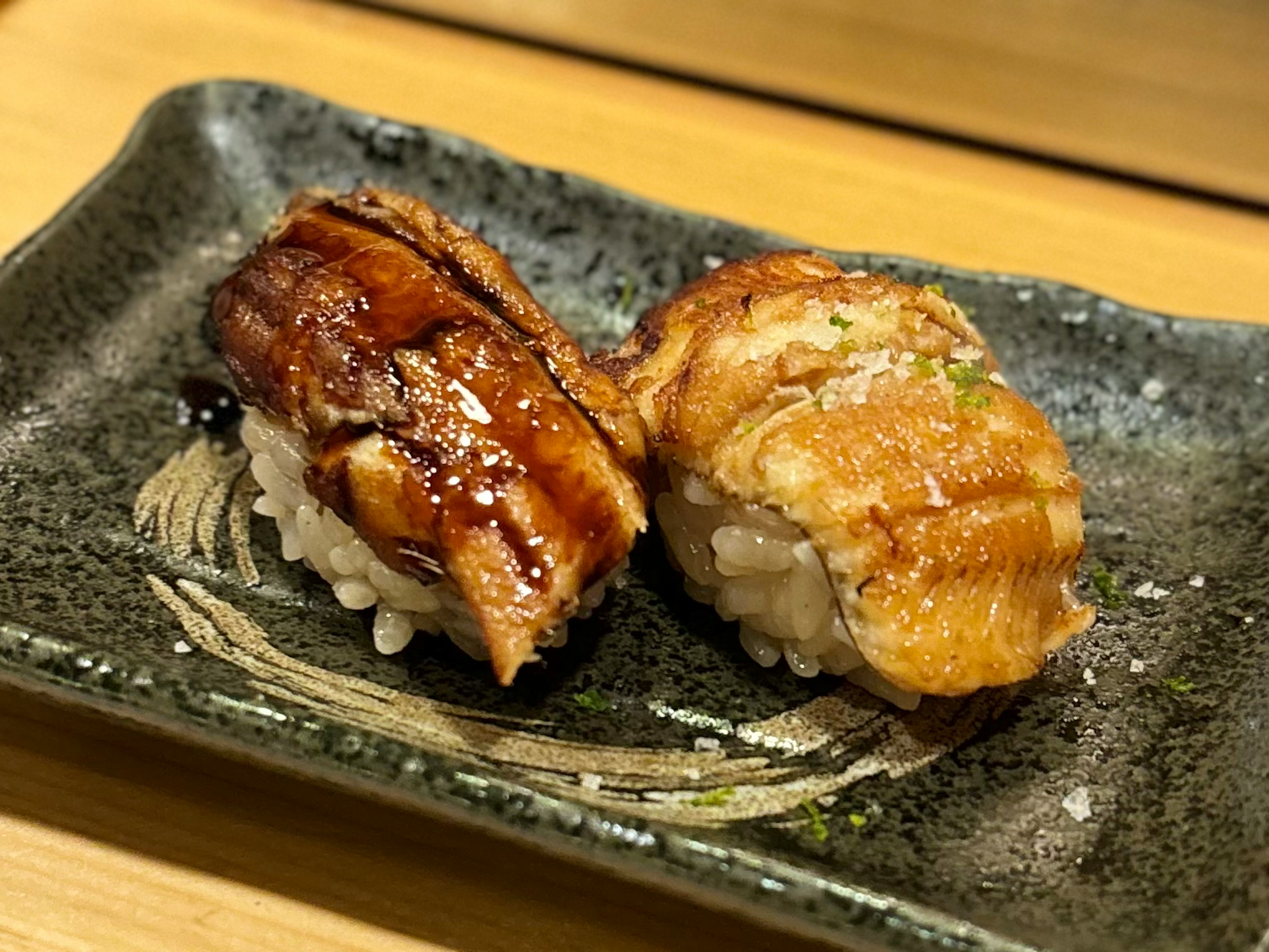 Zwei Stücke gegrilltes Aalsushi auf einem dekorativen Teller präsentiert