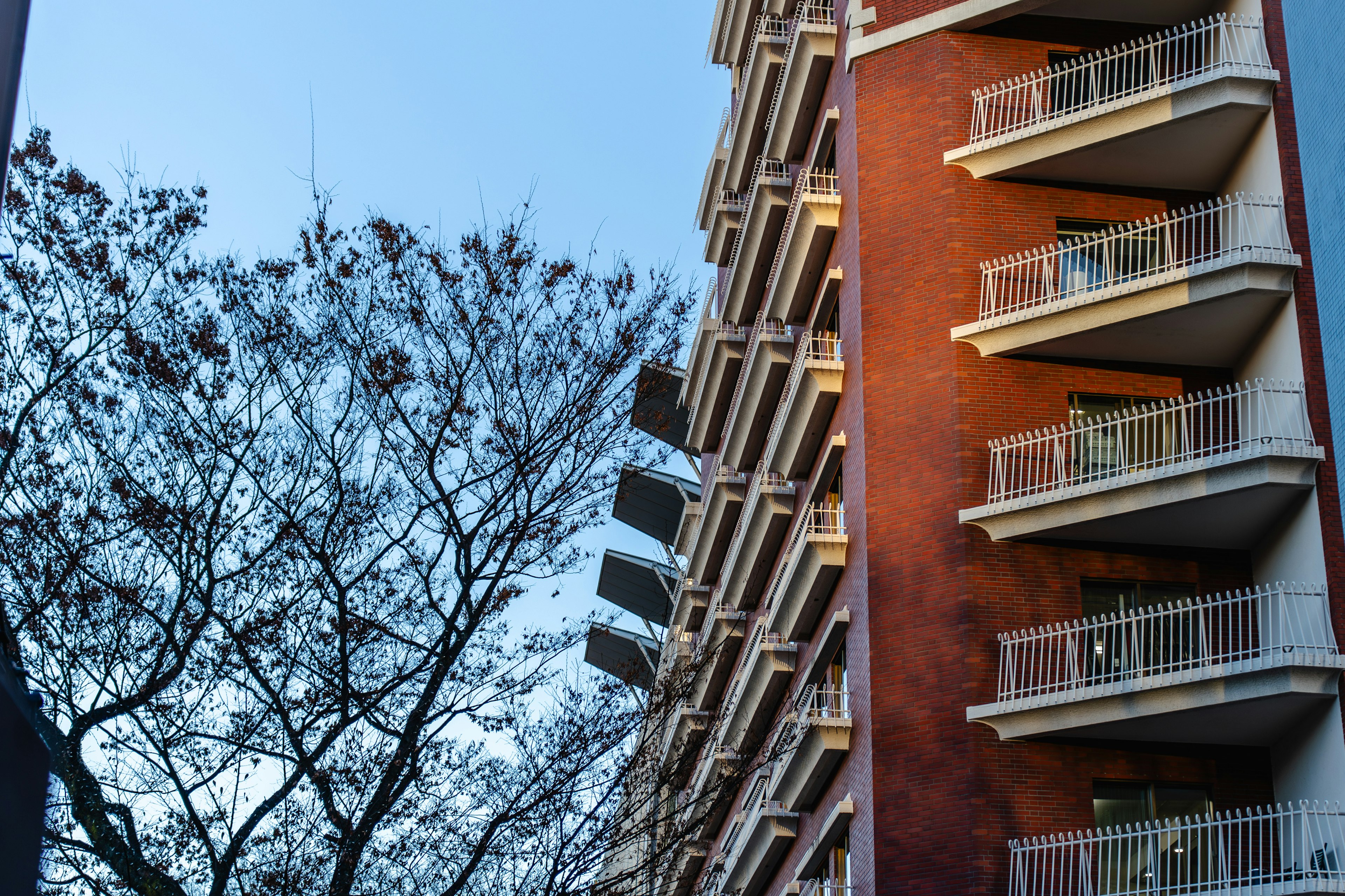 Seitenansicht eines roten Backsteingebäudes mit Balkonen und Silhouette eines Baumes