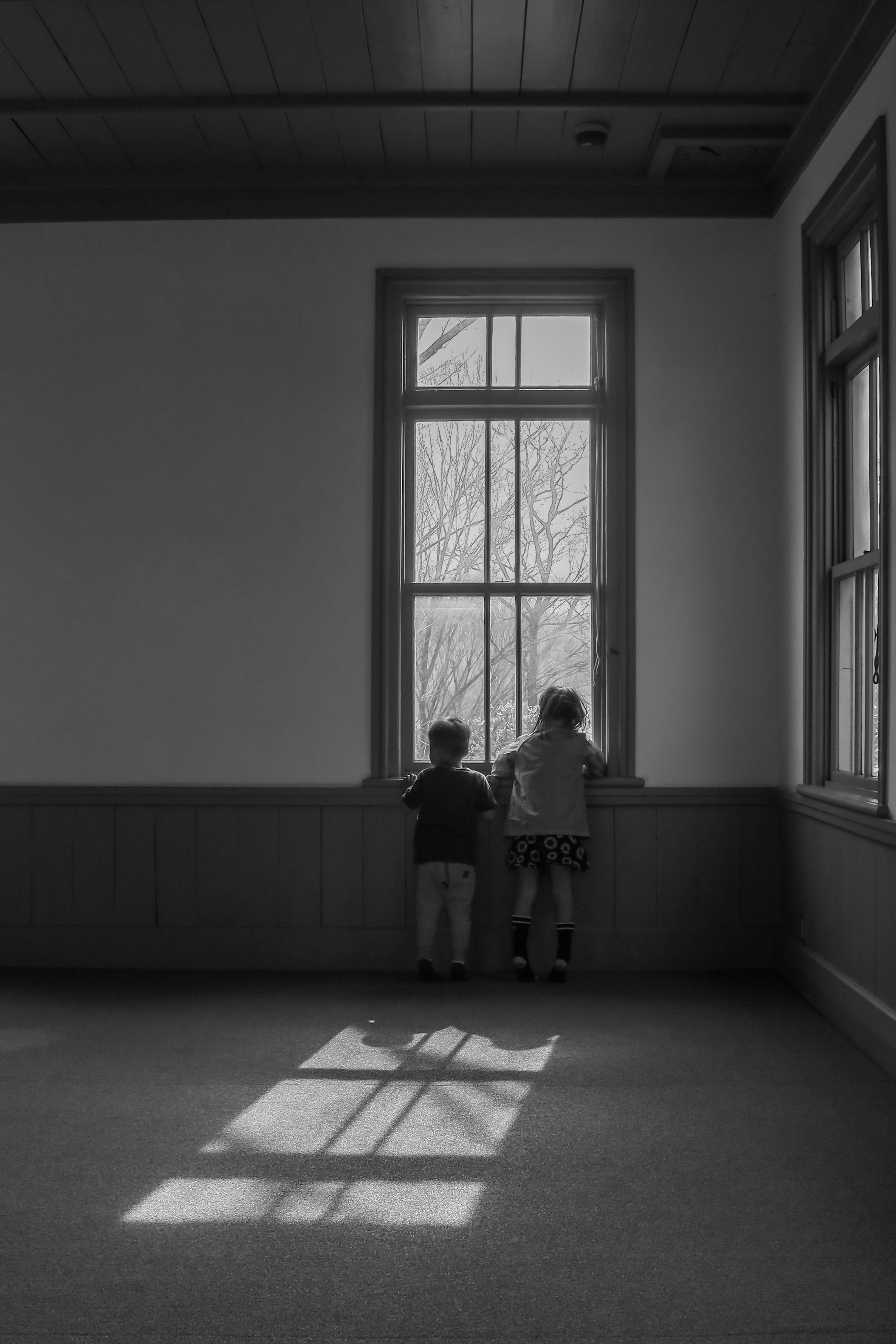 Zwei Kinder schauen aus dem Fenster in einem schwarz-weißen Raum