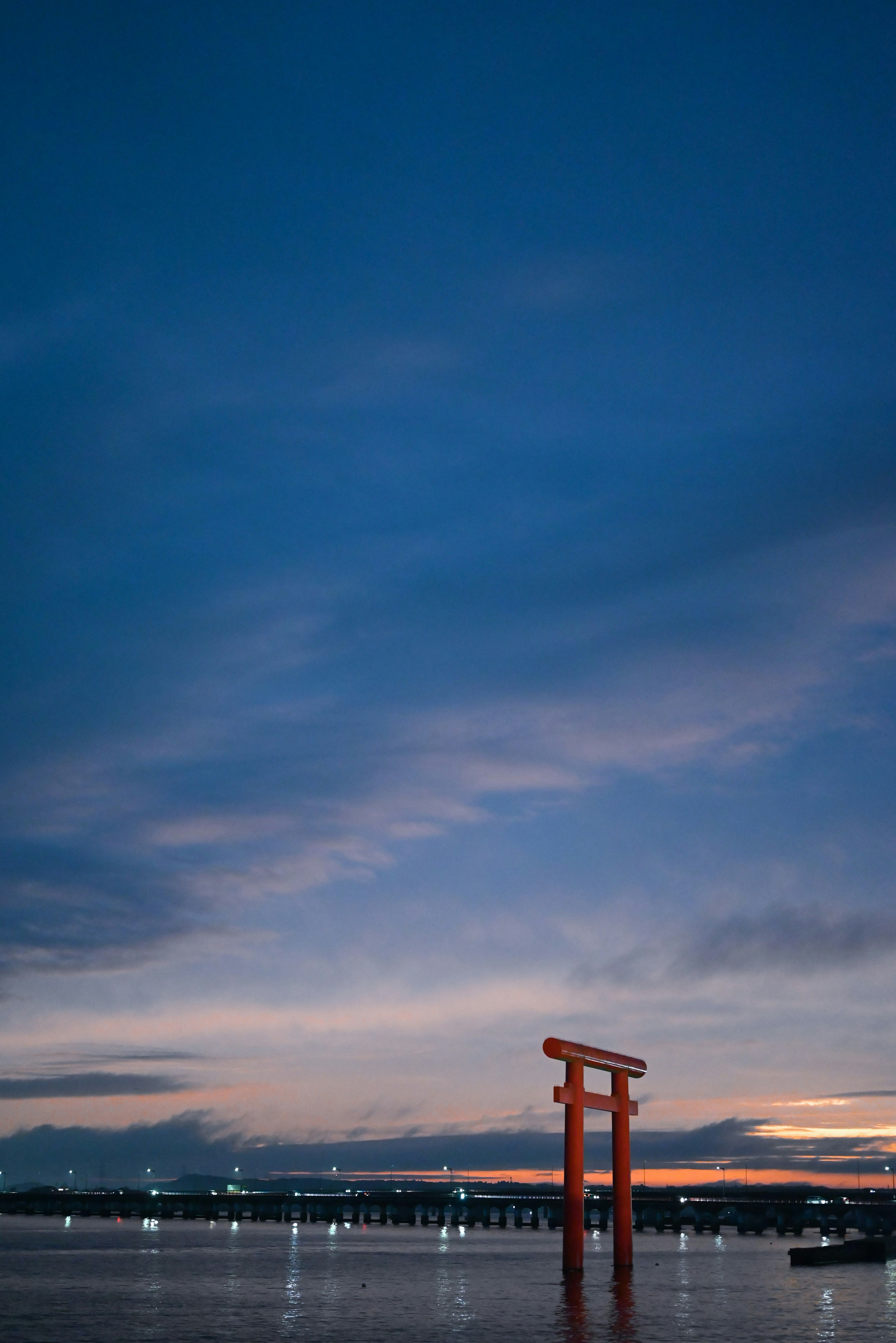 Gerbang torii merah yang memantul di air di bawah langit biru saat senja