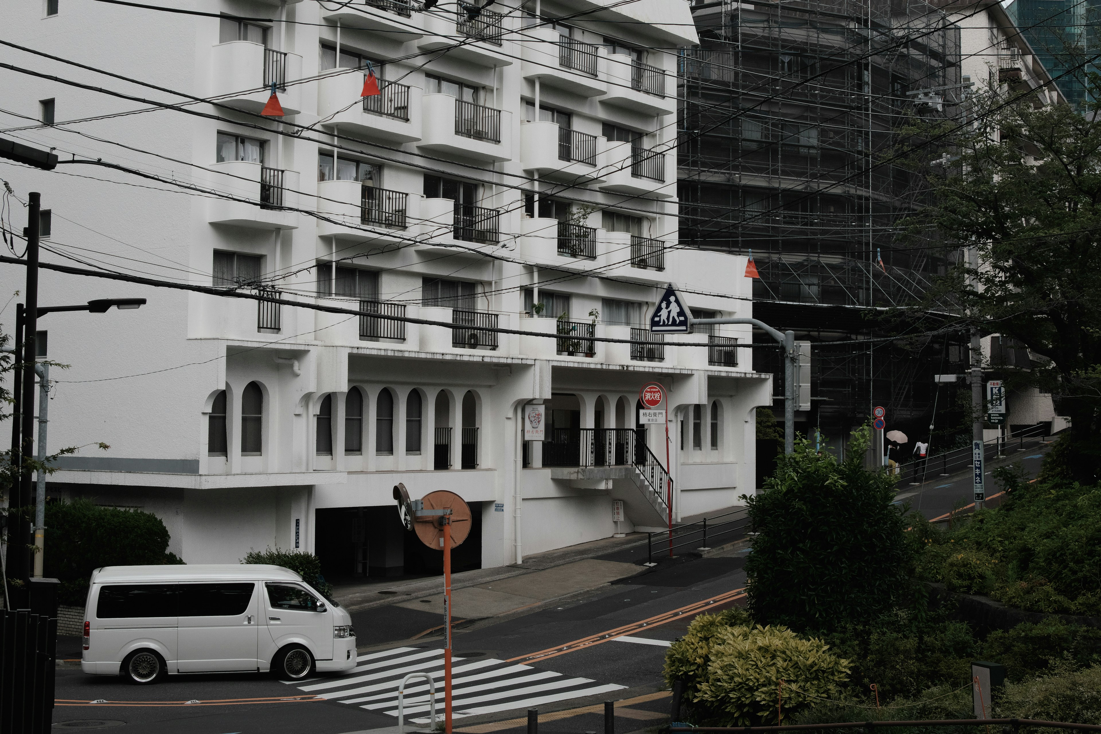 White building with a view of the street featuring a vehicle and greenery