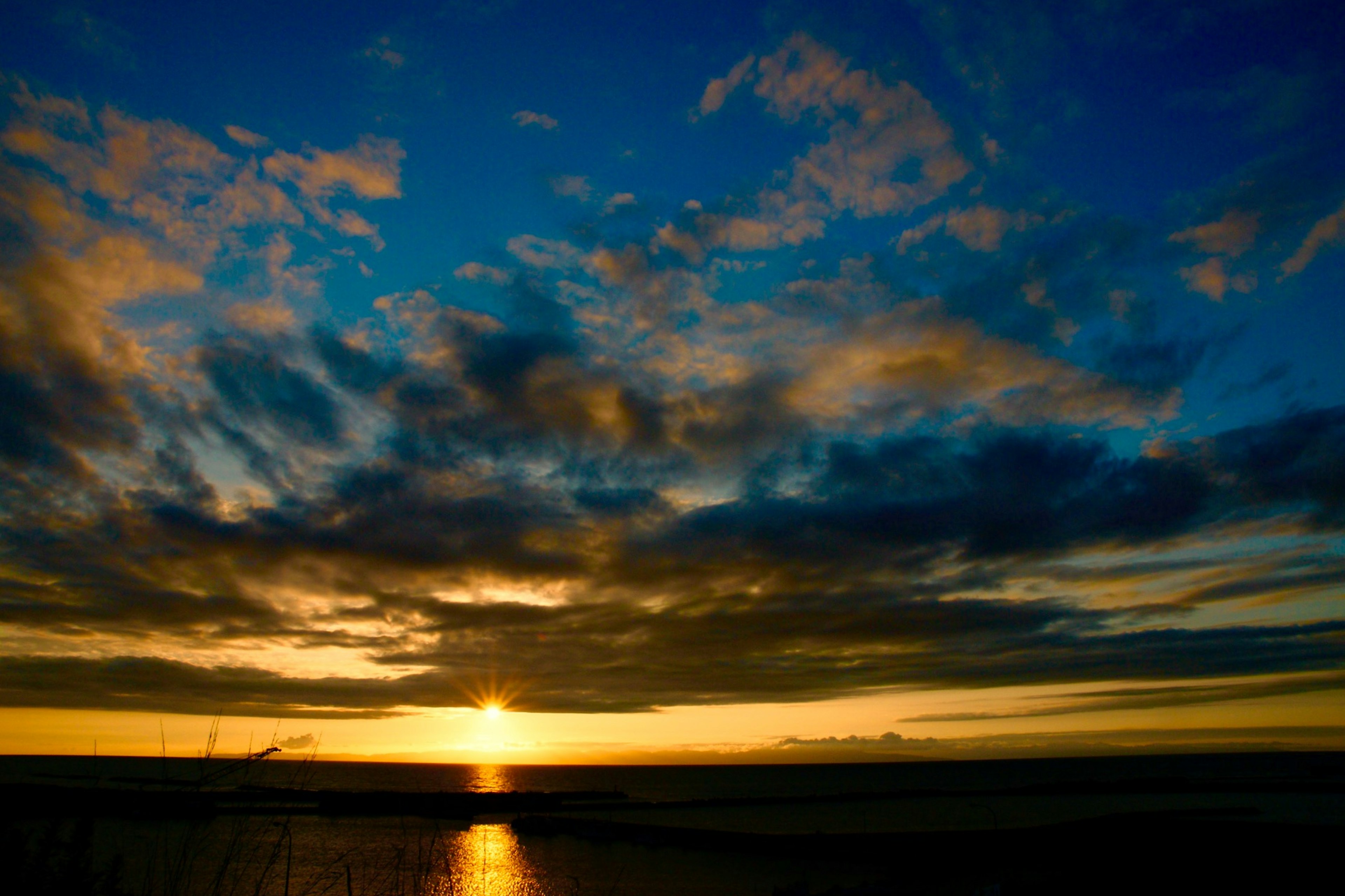 Hermoso atardecer sobre el océano con cielo azul vibrante y nubes naranjas