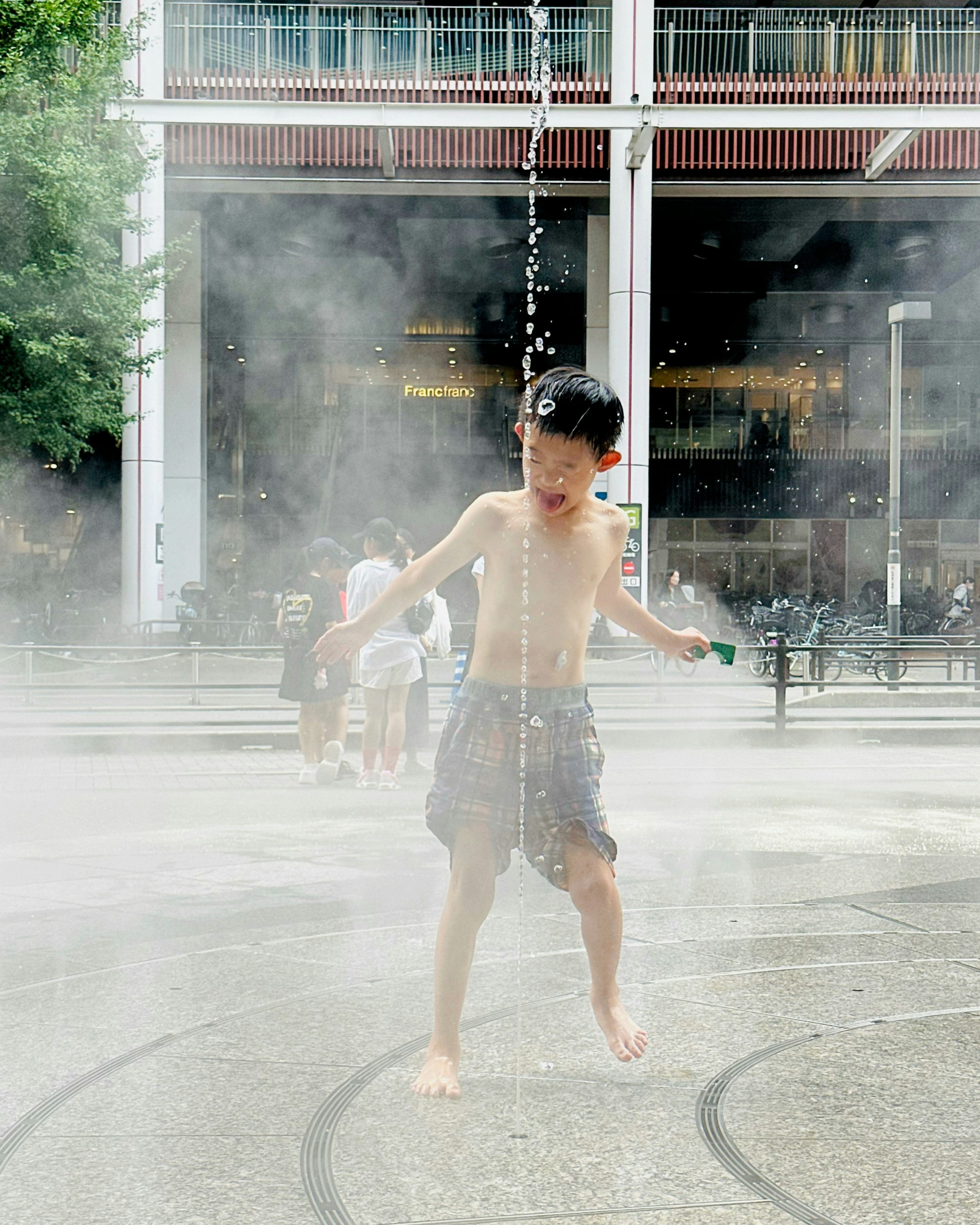 A boy jumping through water jets in a park fountain area