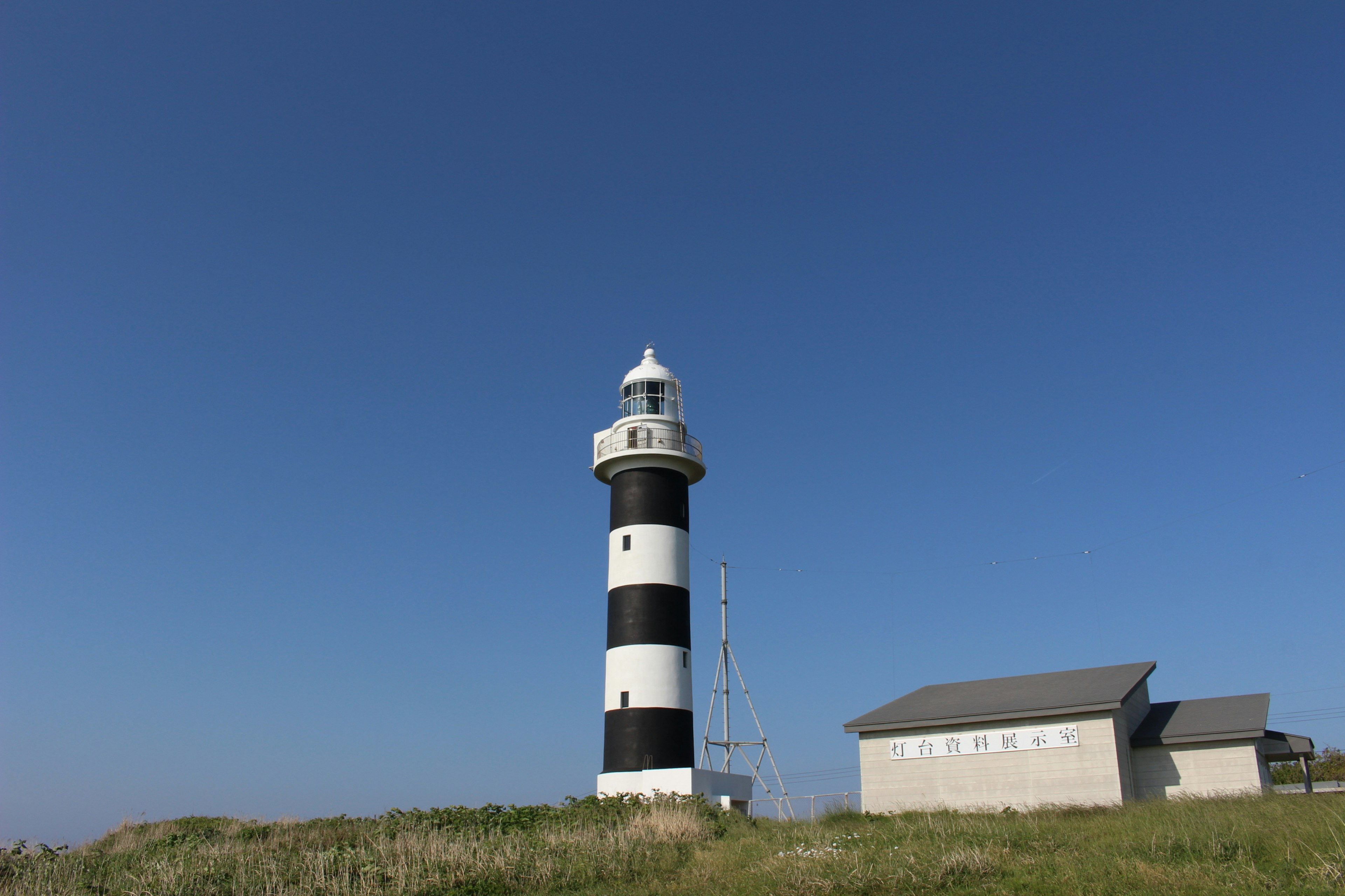 Black and white striped lighthouse under a clear blue sky with an adjacent building